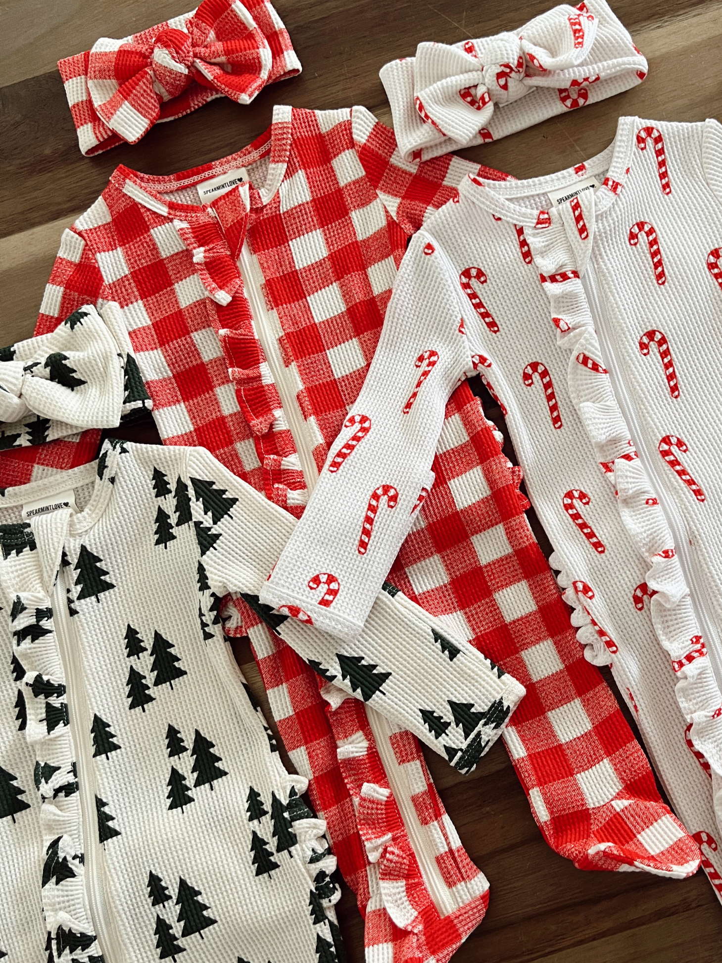Three playful children's outfits with festive patterns: red checkered, white with candy canes, and black forest trees.