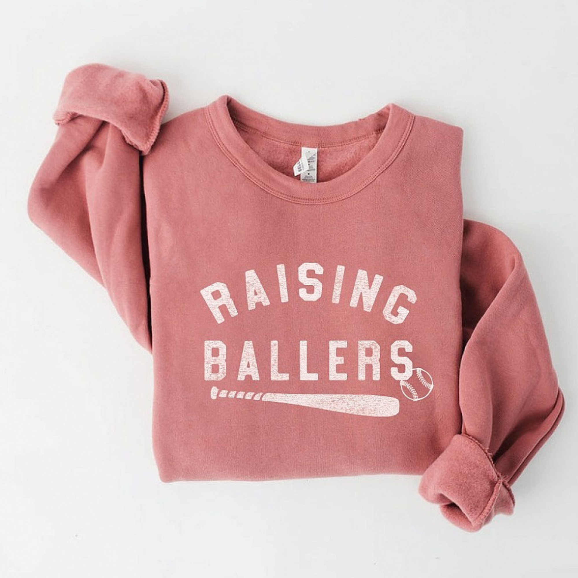 Pink sweatshirt with "Raising Ballers" text and baseball graphics, folded with casual sleeves.