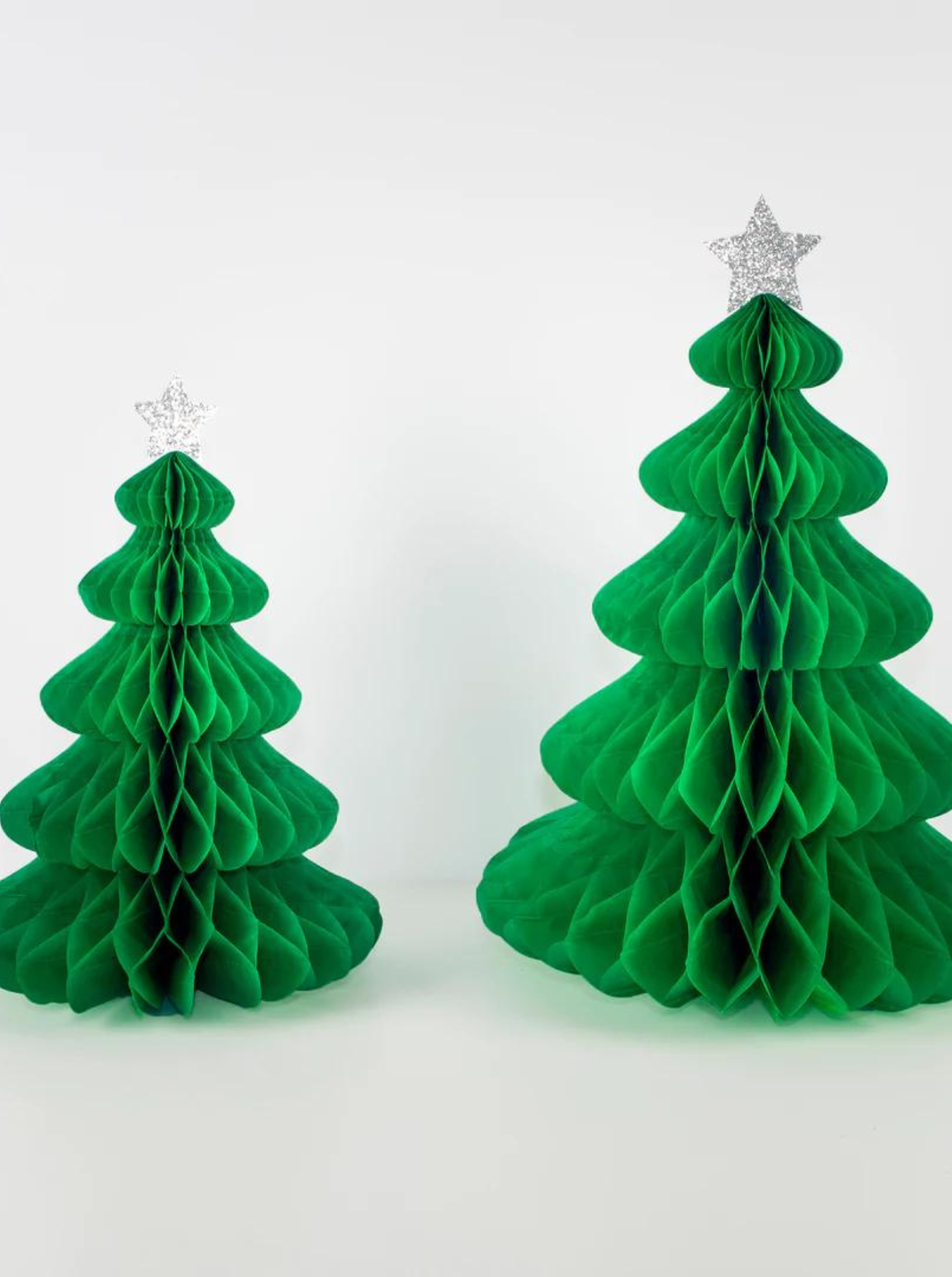 Two green paper honeycomb Christmas trees, one smaller, both topped with silver star ornaments against a white background.