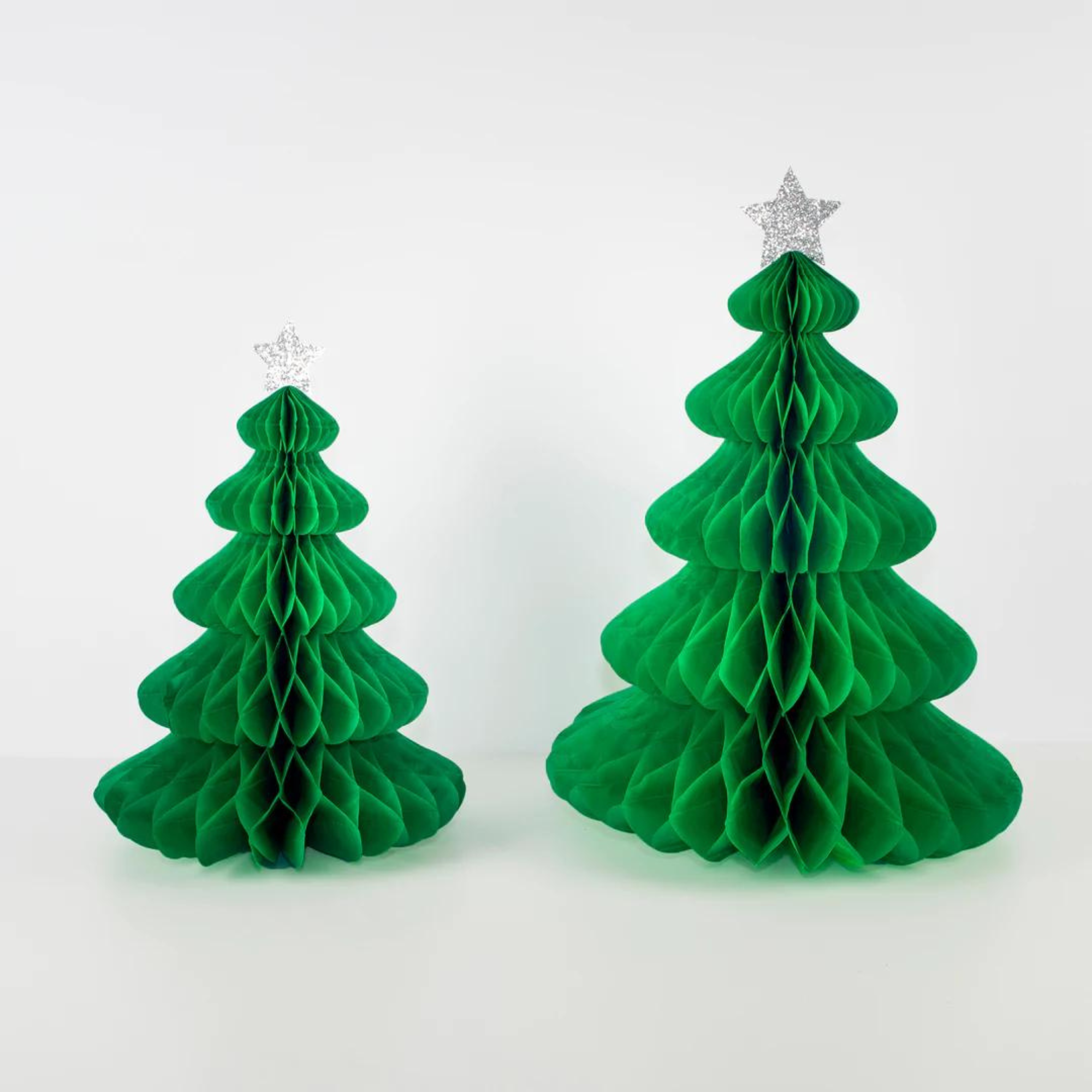 Two green paper honeycomb Christmas trees, one smaller, both topped with silver star ornaments against a white background.