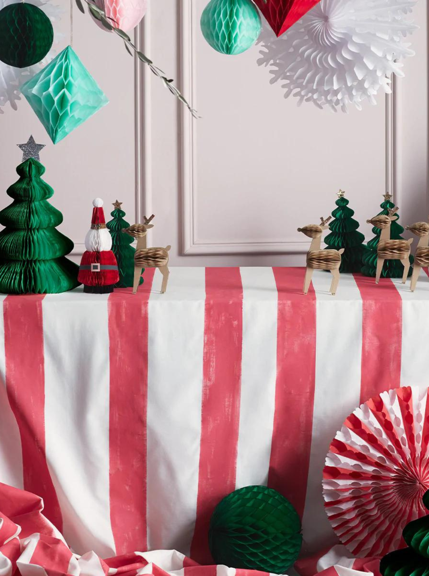 Festive table display with red and white striped cloth, green trees, wooden reindeer, and holiday decorations.
