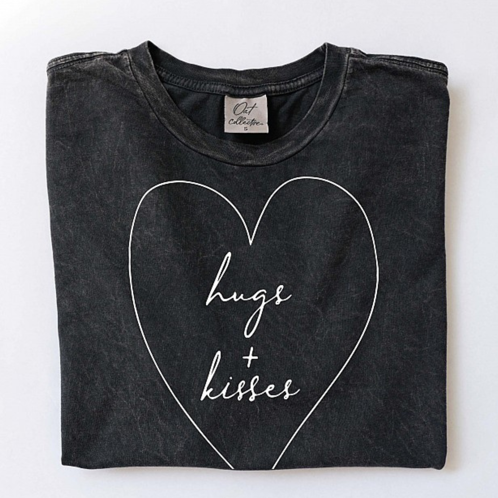 Black t-shirt folded with "hugs + kisses" in a white heart design. Casual and stylish graphic apparel.