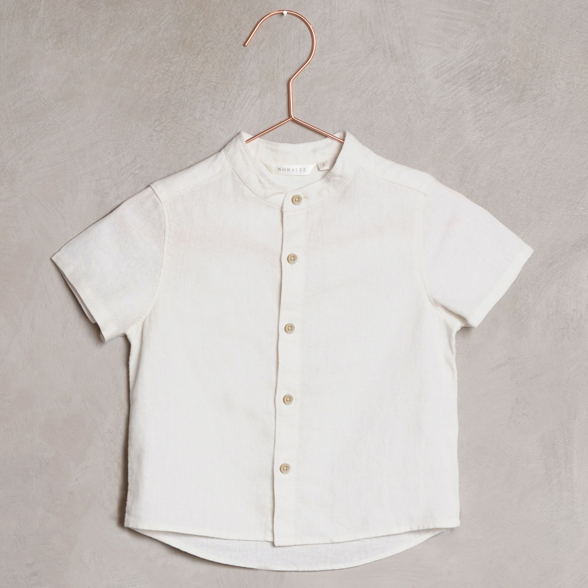 Short-sleeve white button-up shirt hanging on a copper hanger against a textured background.
