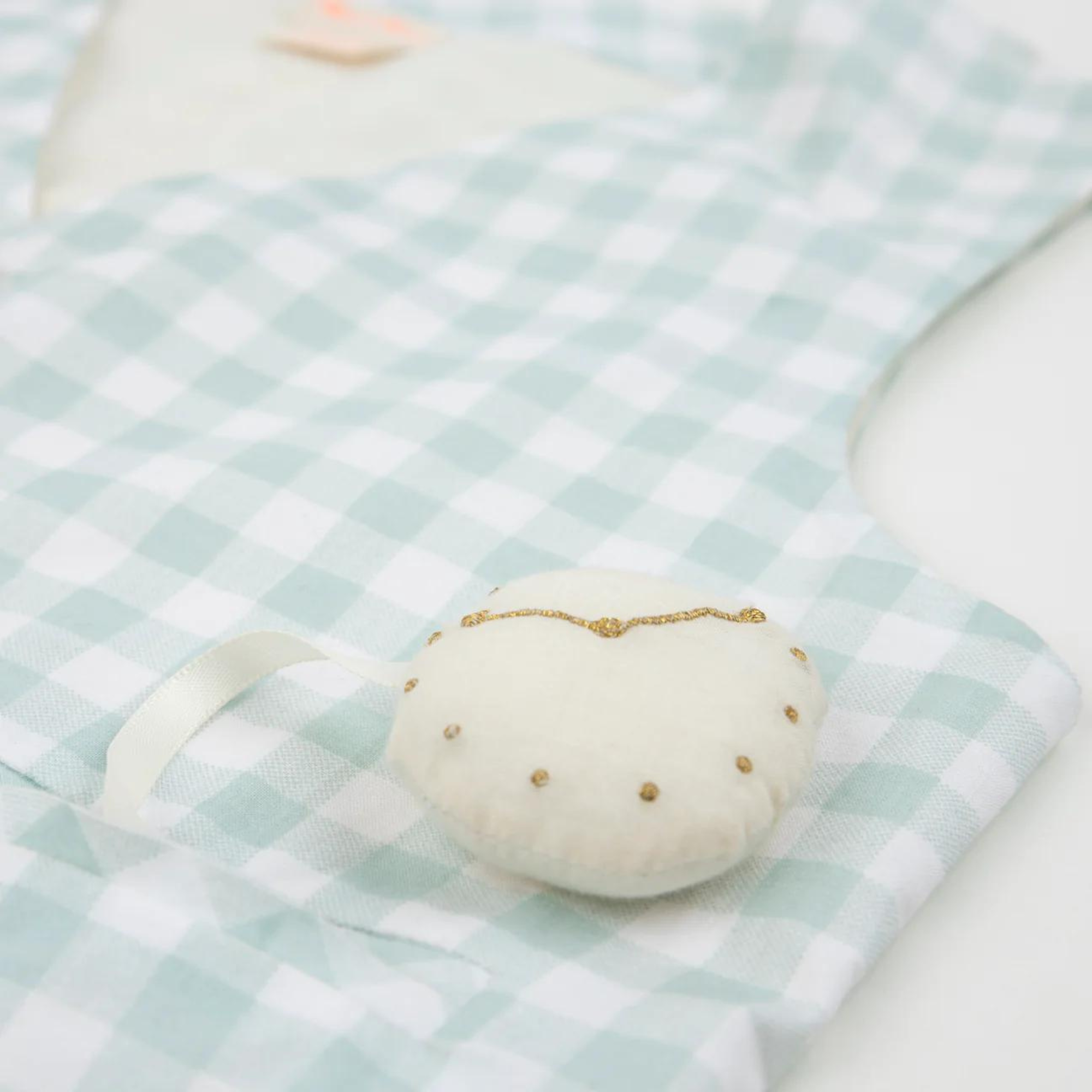 Close-up of a light blue and white checkered fabric with a cream-colored pin cushion.