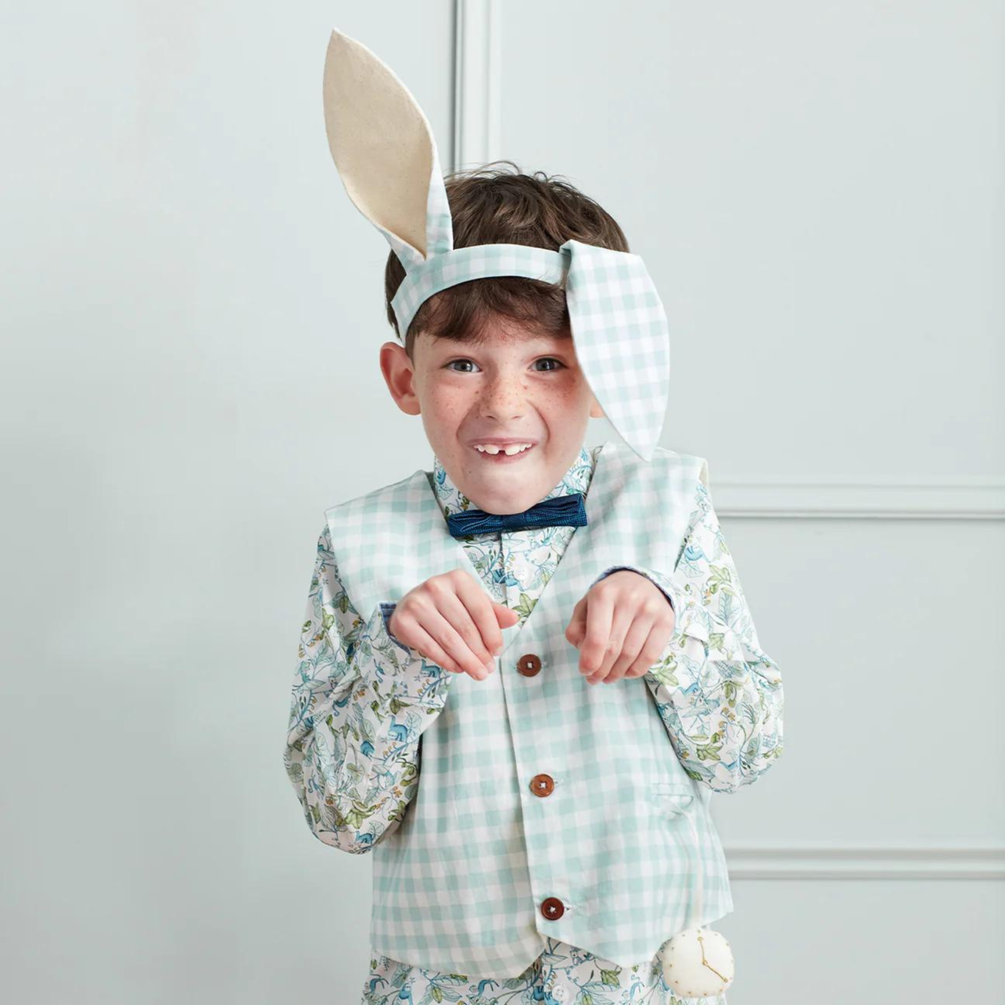 Boy in bunny costume with ears and bow tie, playfully posing against a light background.
