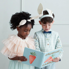 Two children in bunny outfits read a book titled "Growing Carrots," showcasing joy and curiosity.