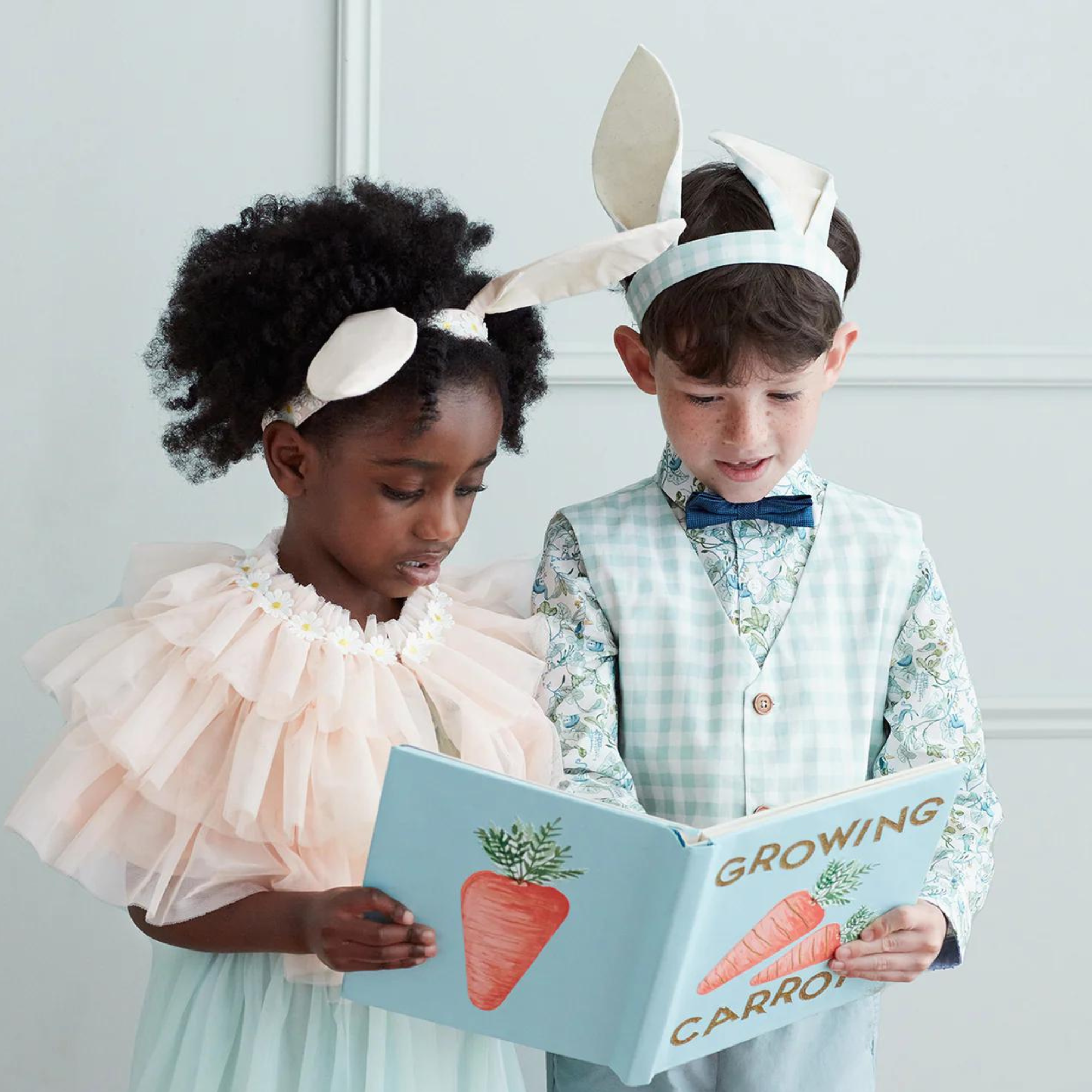Two children in bunny outfits read a book titled "Growing Carrots," showcasing joy and curiosity.