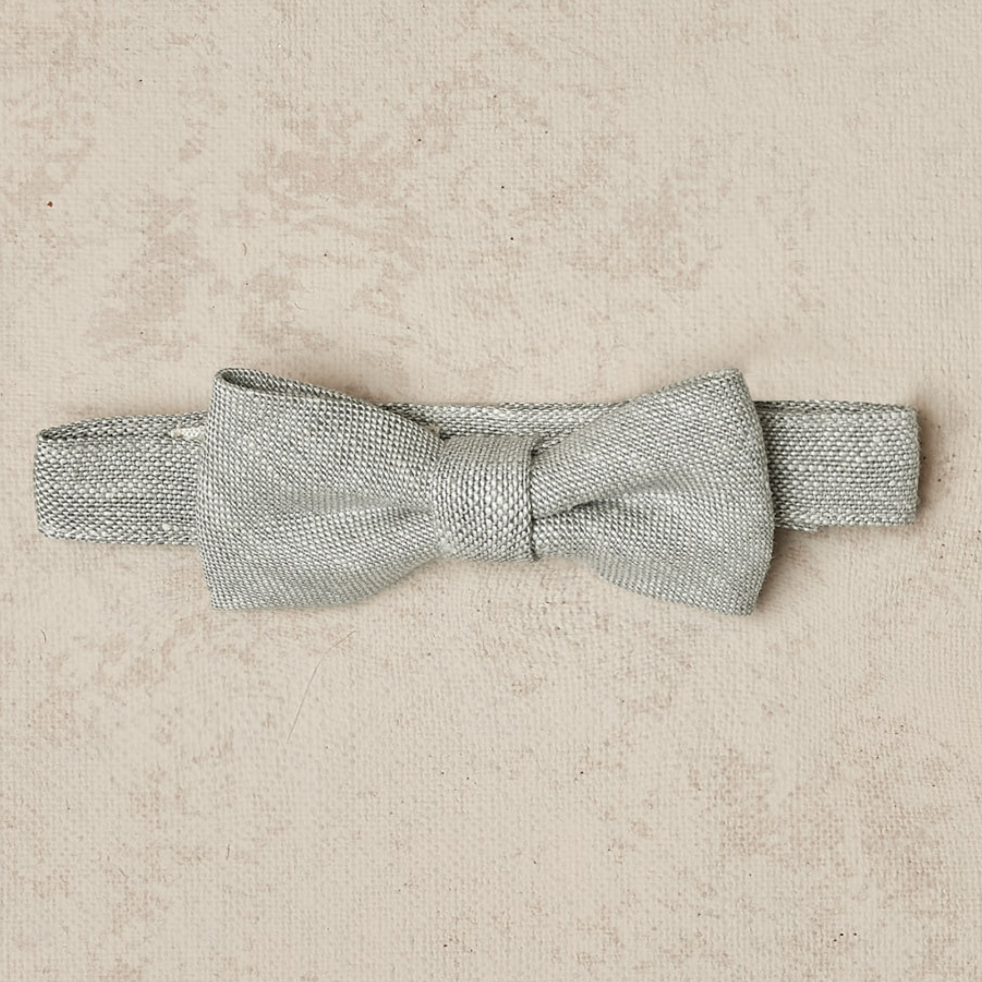 Silver bow tie on a light textured background, designed for formal wear or special occasions.
