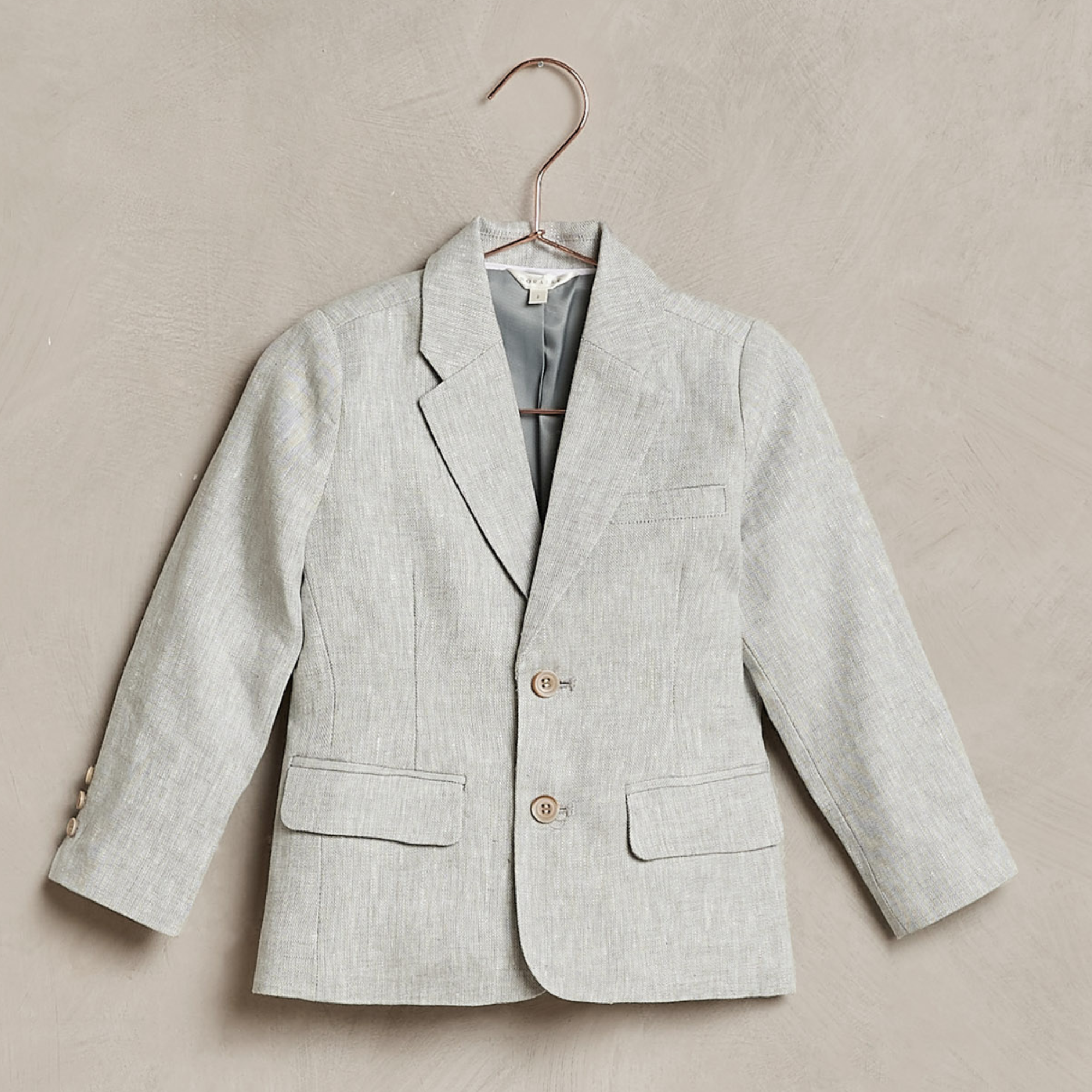 Light gray children's blazer on a hanger against a textured background.