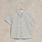 Short-sleeve green and white checkered shirt hanging on a copper hanger against a textured background.