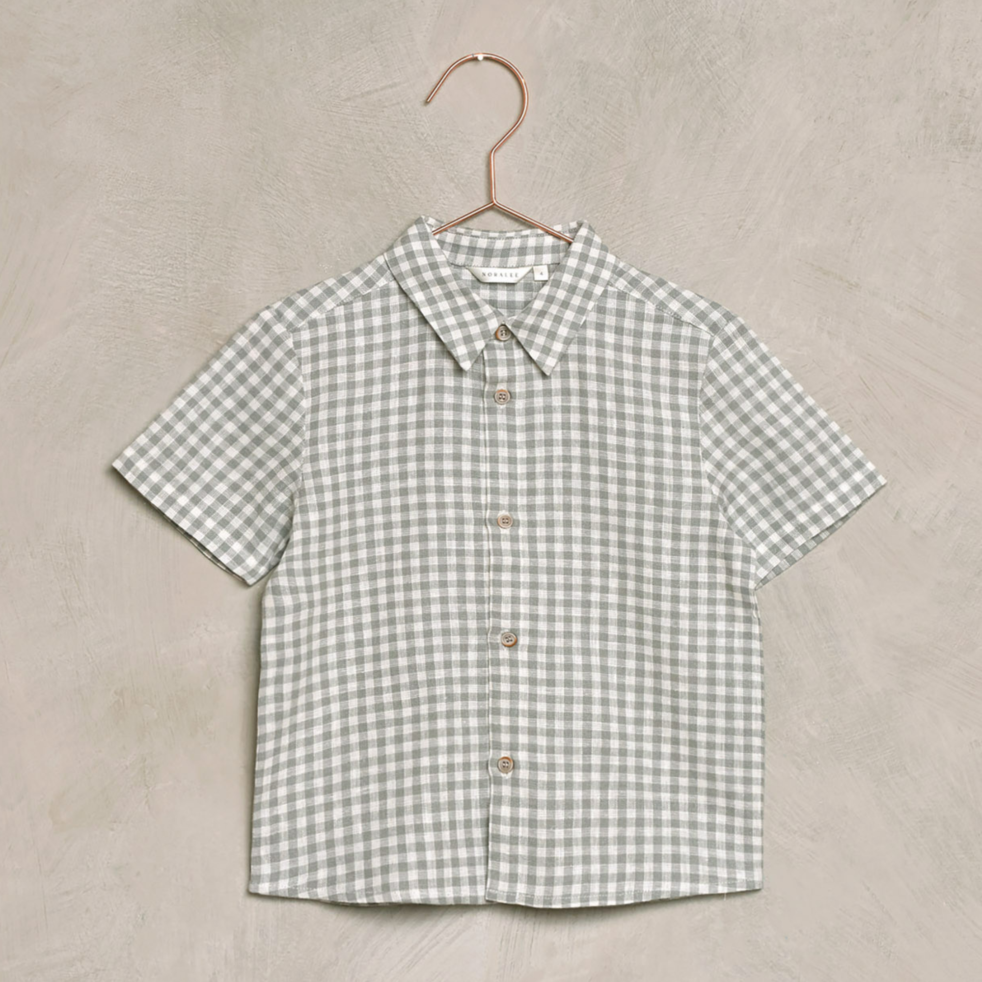 Short-sleeve green and white checkered shirt hanging on a copper hanger against a textured background.