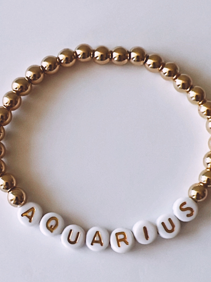 Gold and white beaded bracelet with the word "AQUARIUS" spelled out.