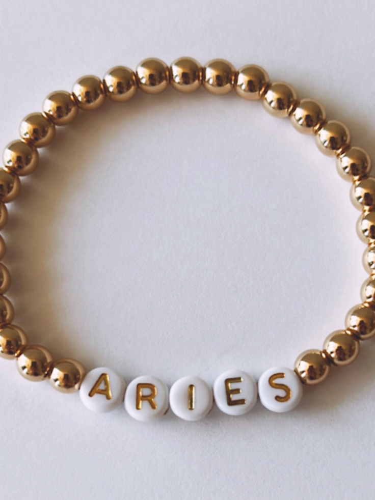 Gold and white beaded bracelet with "ARIES" spelled out in letter beads.