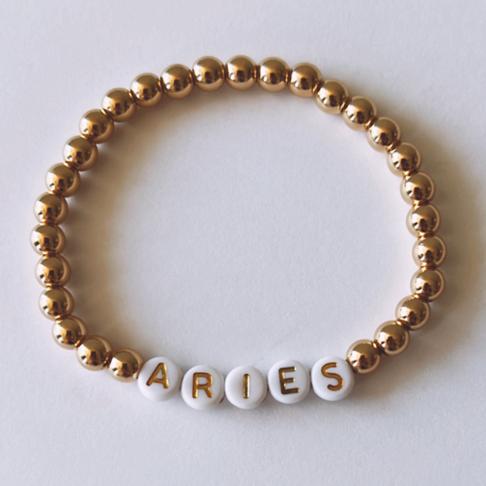 Gold and white beaded bracelet with "ARIES" spelled out in letter beads.