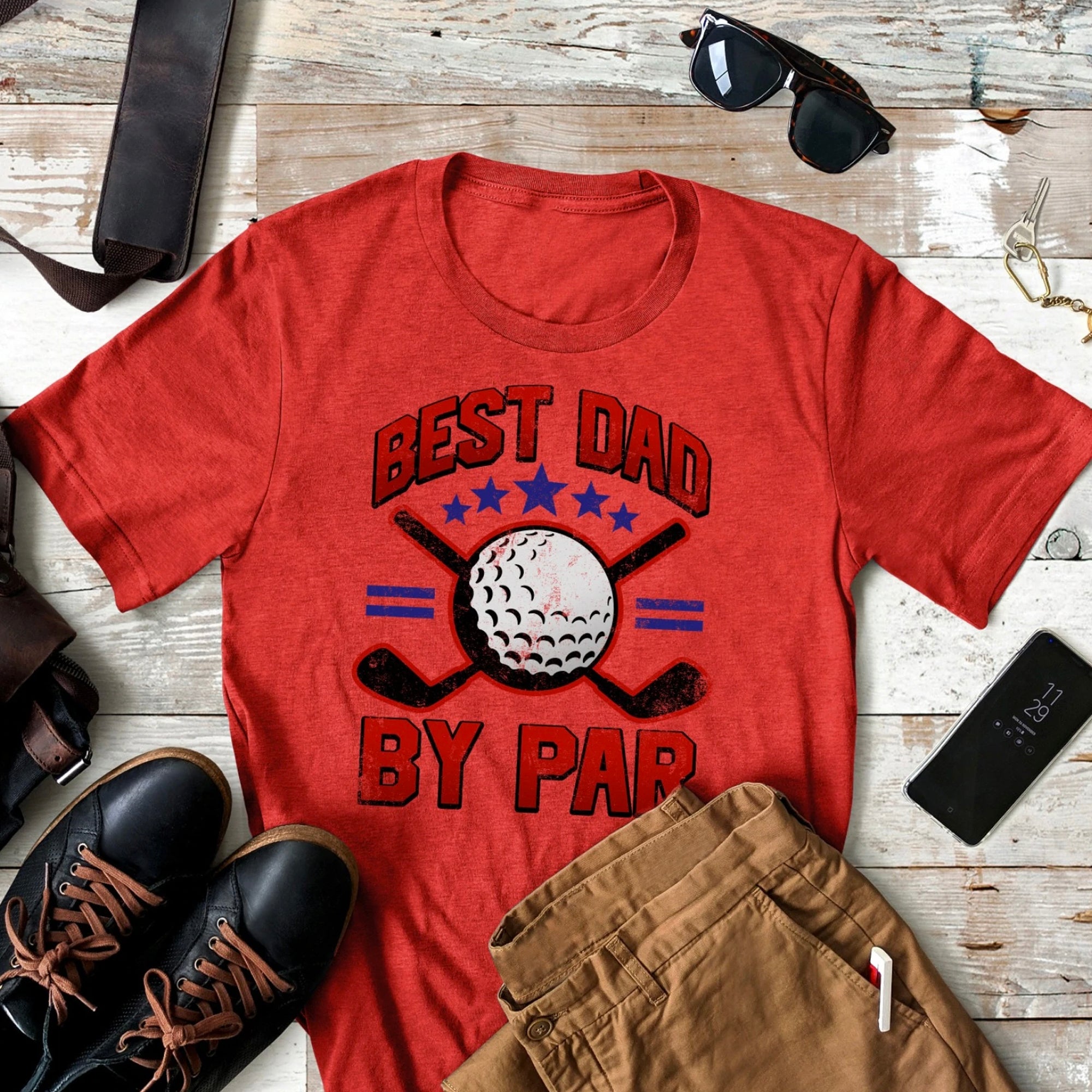 Red t-shirt with "Best Dad By Par" graphic, golf ball, and crossed clubs, styled with casual accessories.