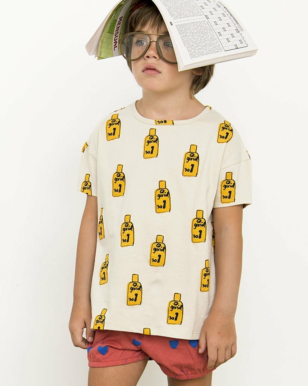Child wearing a patterned shirt with yellow bottle illustrations, holding a book above their head.