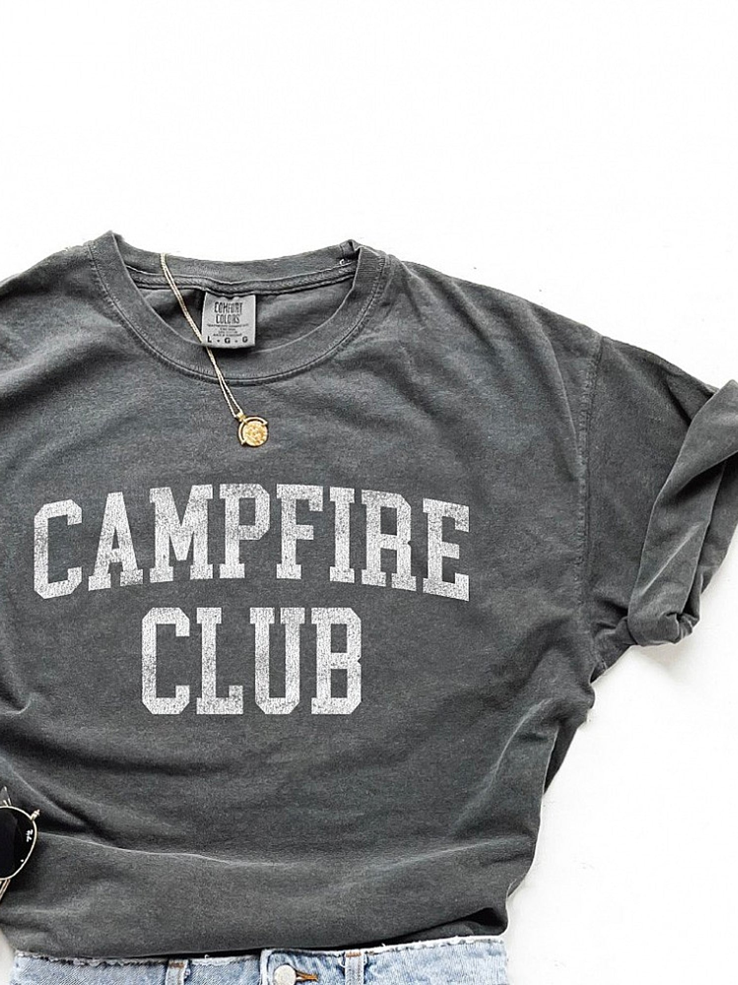 Gray t-shirt with "CAMPFIRE CLUB" printed in bold white letters, styled with accessories.