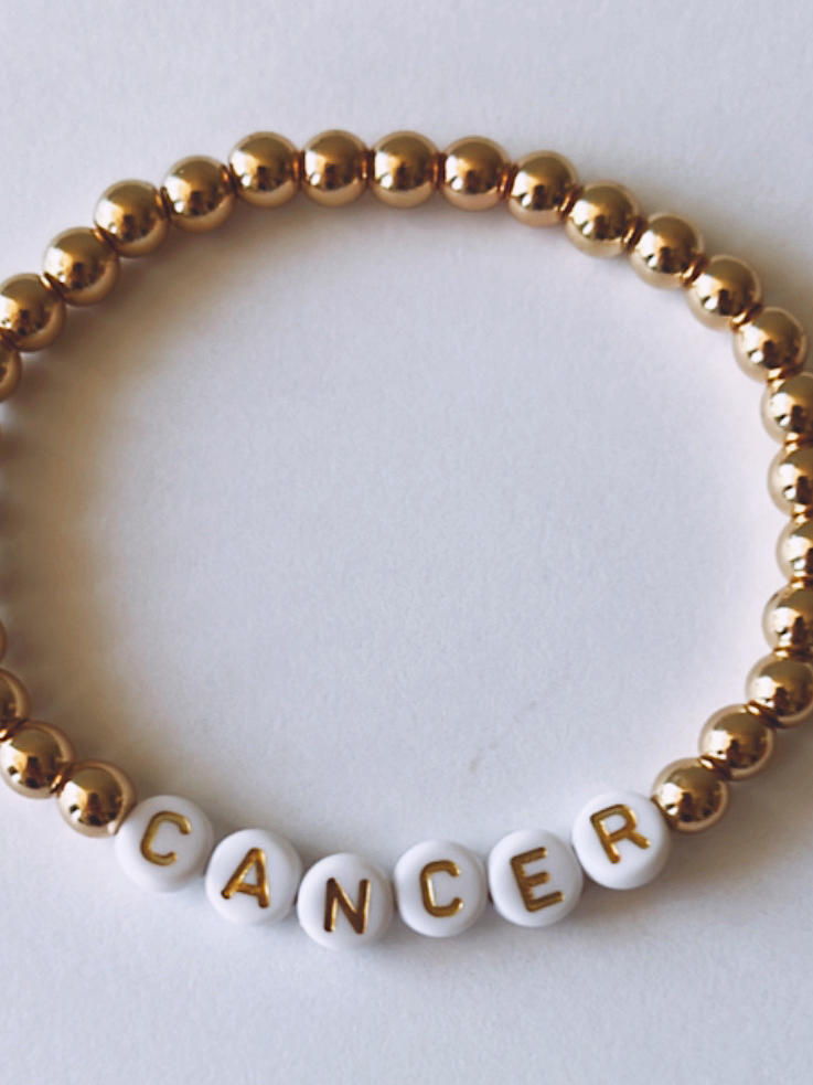 Gold and white bead bracelet with the word "CANCER" spelled out in white letters.