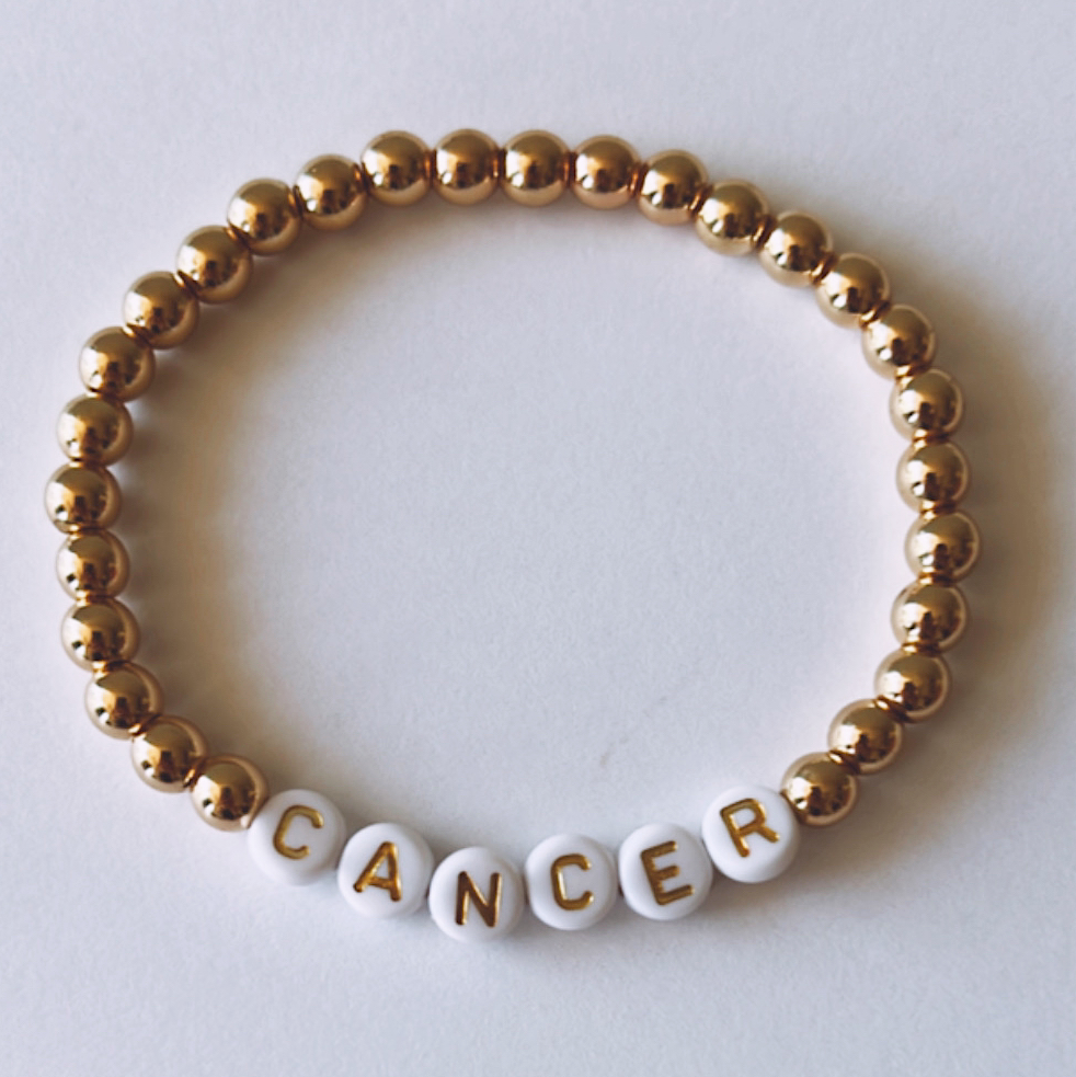Gold and white bead bracelet with the word "CANCER" spelled out in white letters.