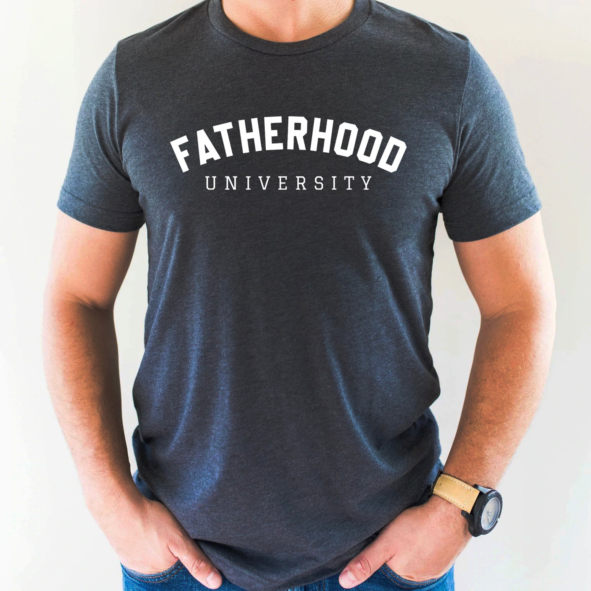 Man wearing a dark gray t-shirt with "Fatherhood University" printed in white letters. Casual attire for dads.