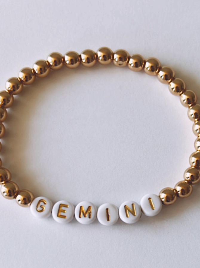 Gold and white beaded bracelet featuring the letters spelling "GEMINI."