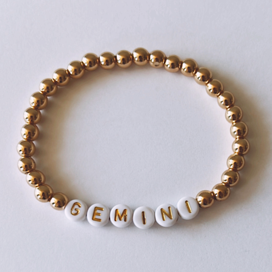 Gold and white beaded bracelet featuring the letters spelling "GEMINI."