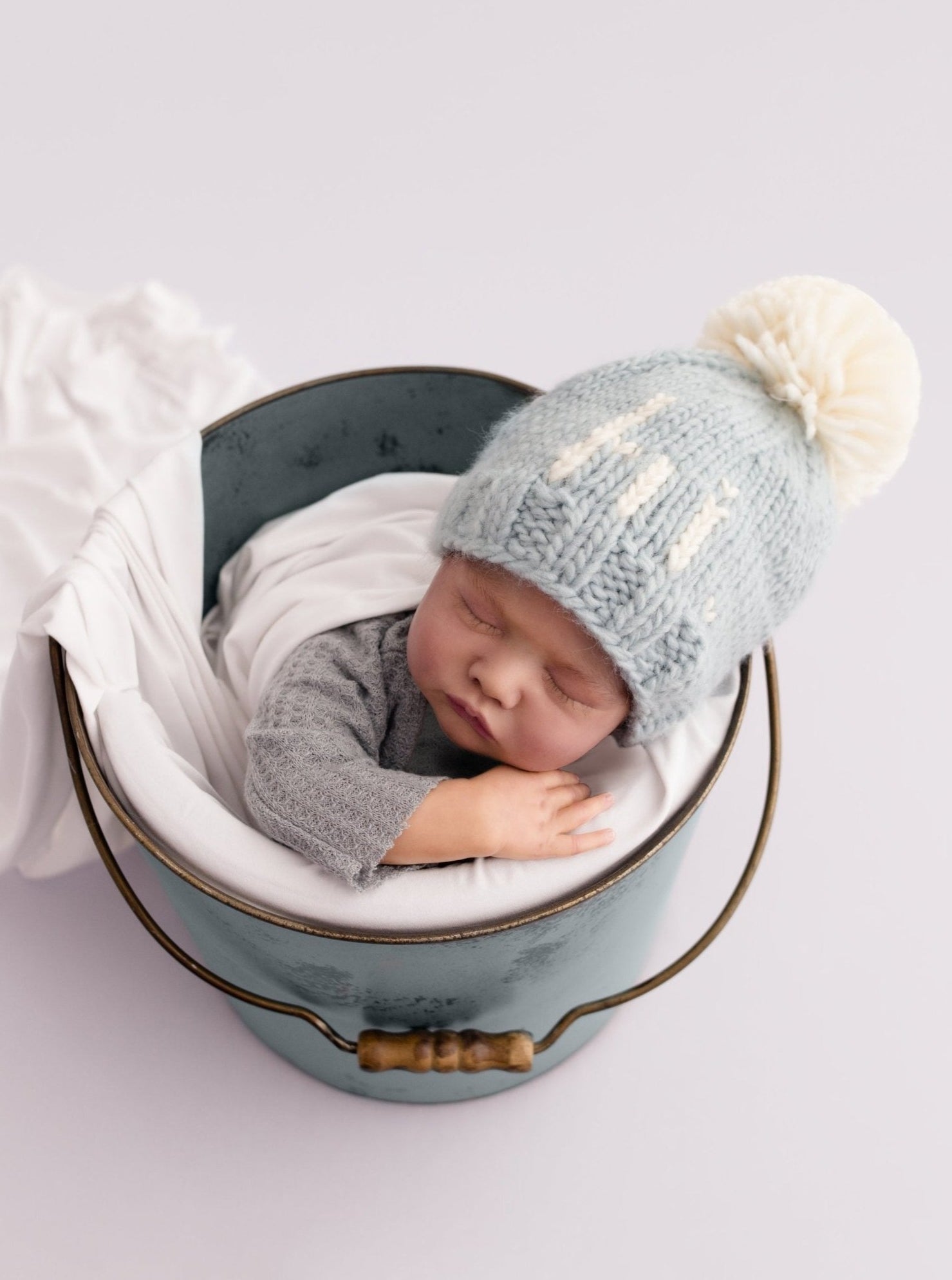 Newborn baby peacefully sleeping in a bucket, wearing a cozy knit hat and wrapped in a soft blanket.