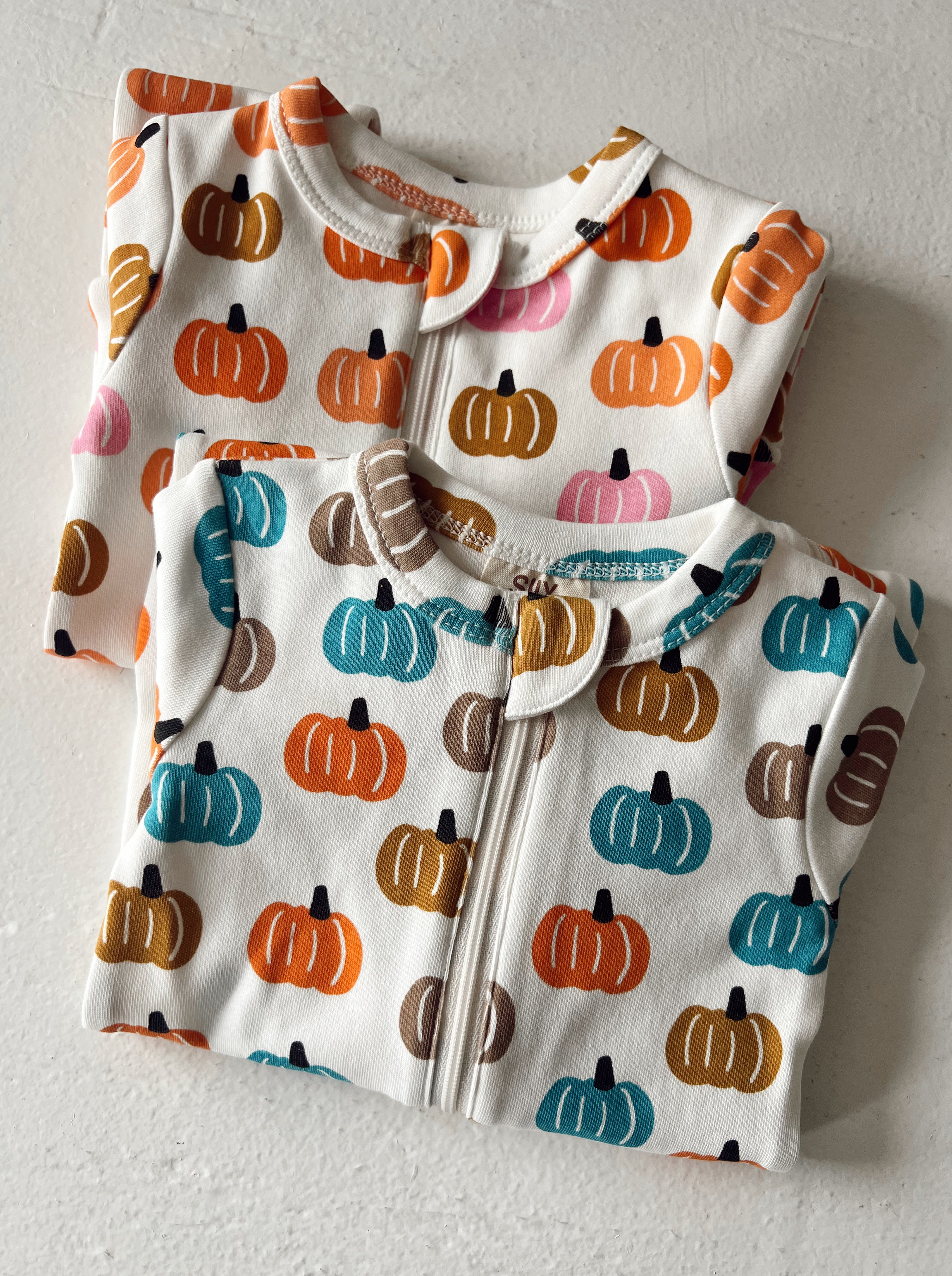 Two children's pajamas with colorful pumpkin patterns on a light background.