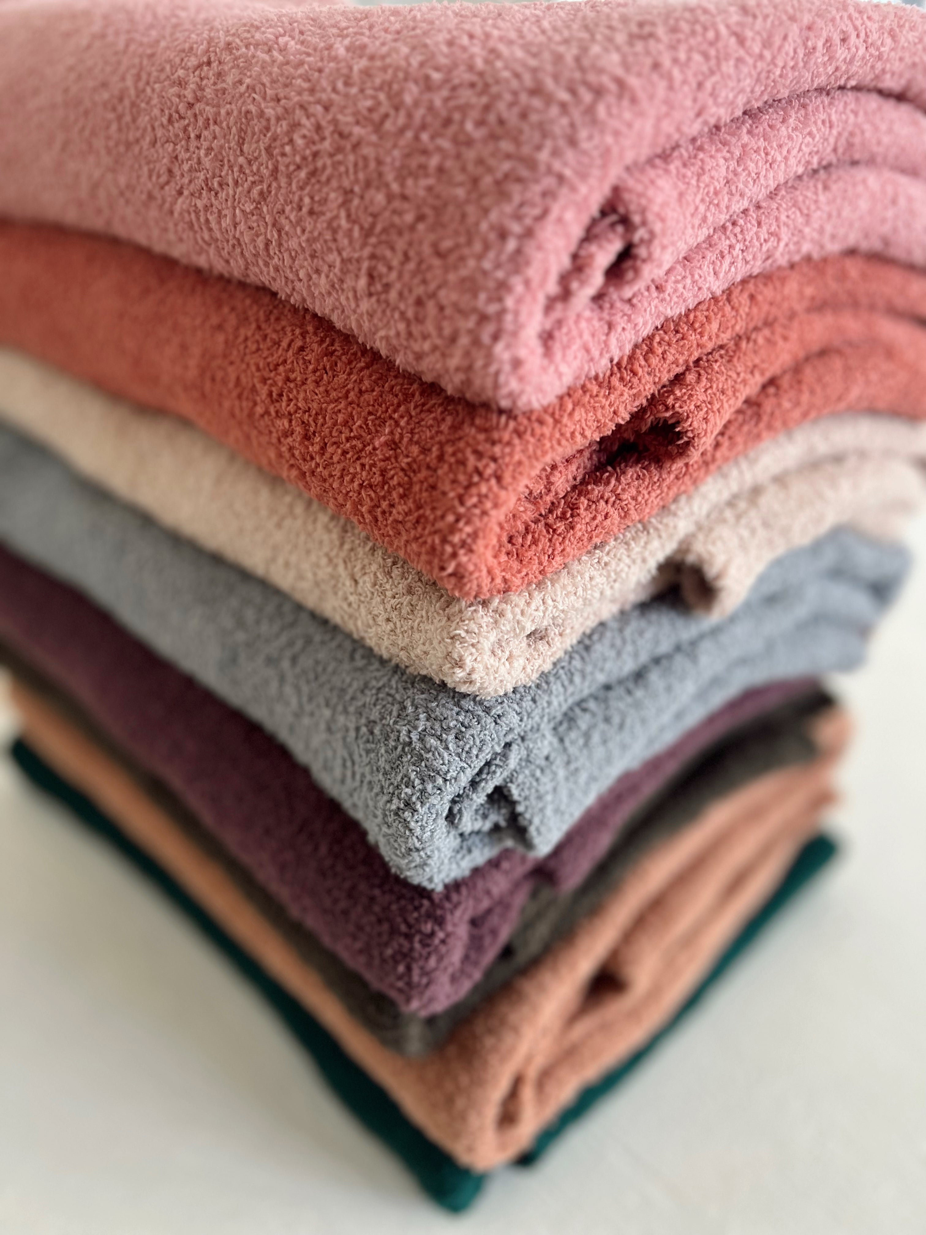 Stack of colorful, soft towels in shades of pink, orange, gray, and purple, neatly folded on a white surface.