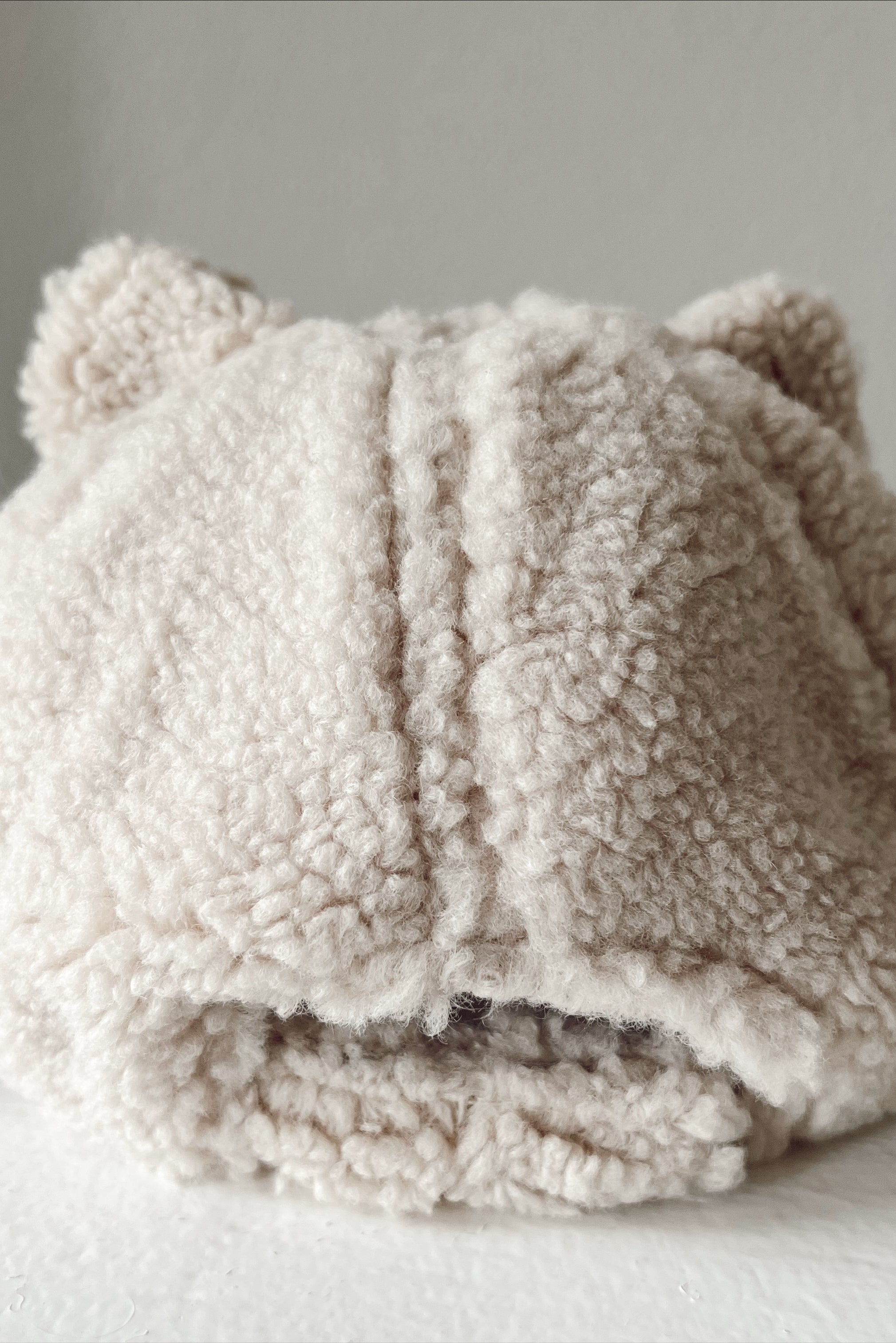 Beige fluffy hat with cat ears, displayed from the back on a light surface.