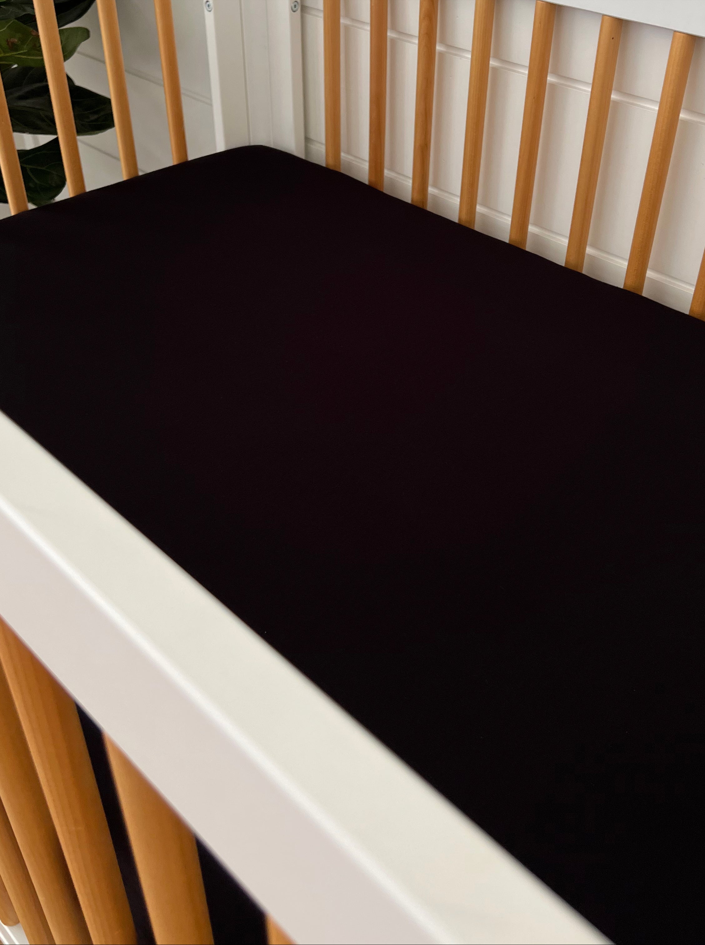 Black crib mattress in a modern crib with wooden slats and a floral background.