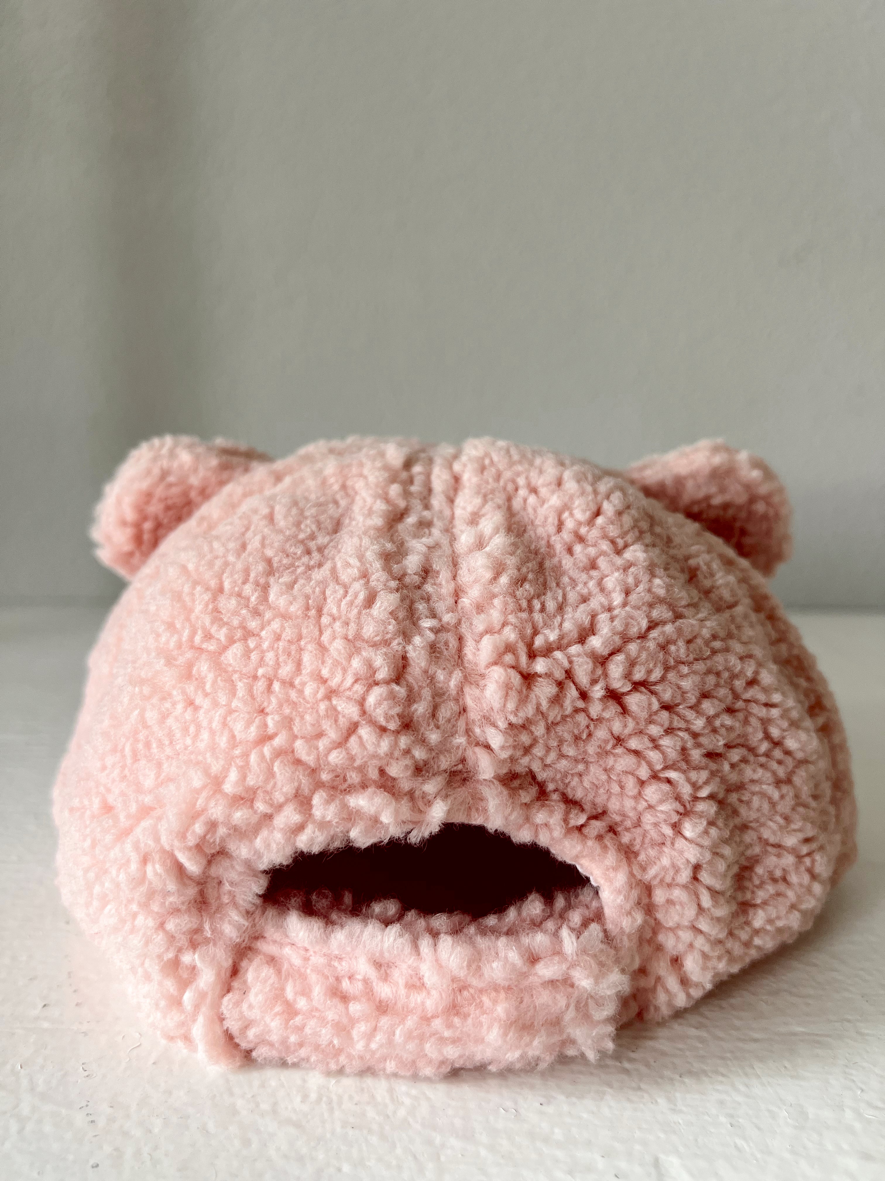 Pink fuzzy hat with bear ears, featuring a round opening at the front, displayed on a light background.
