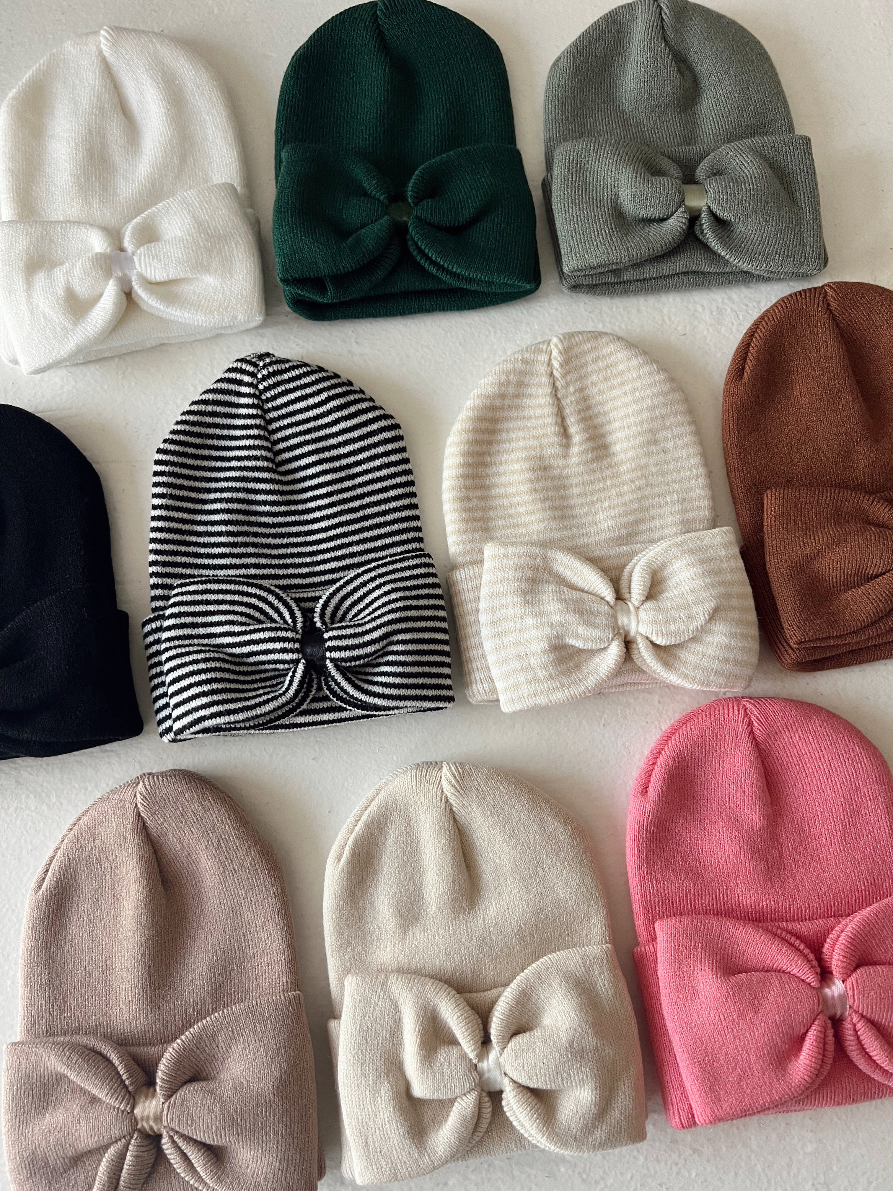 Various colorful beanies with bows arranged in a grid on a white surface.