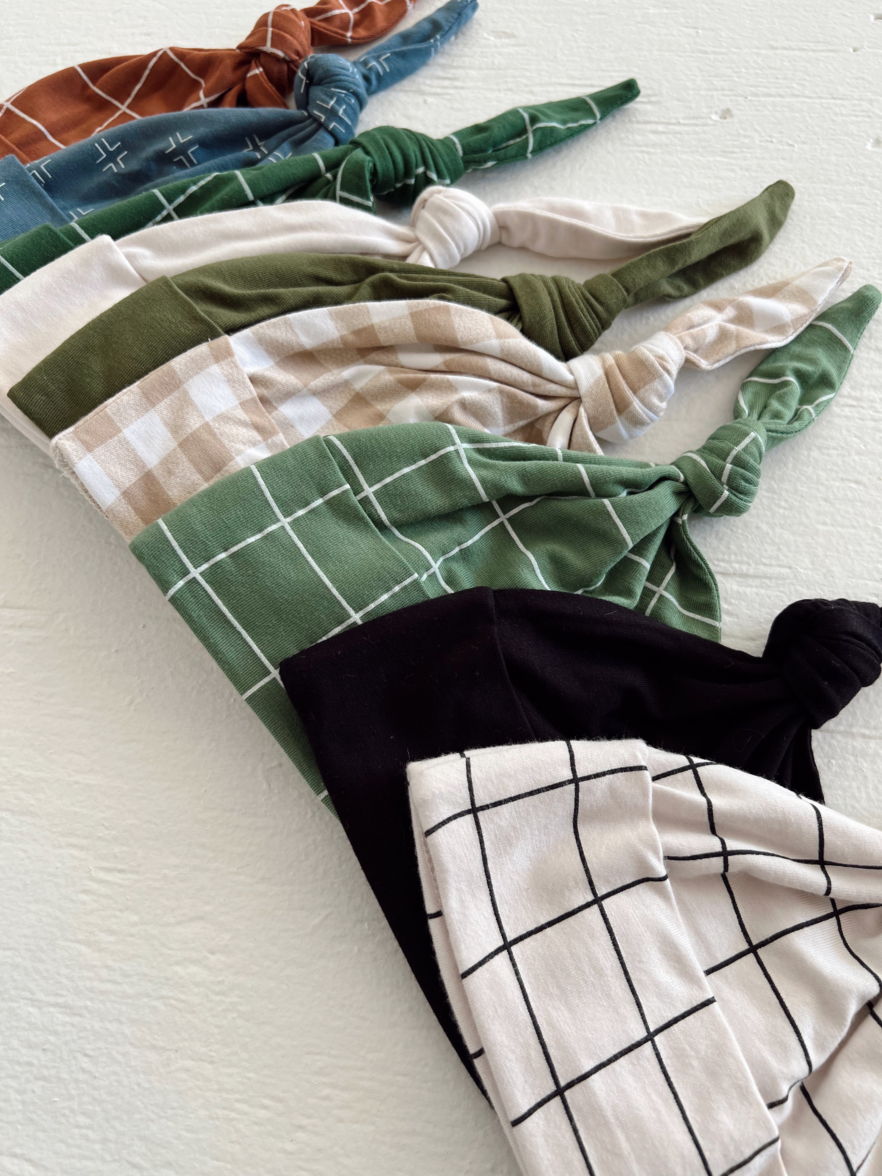 A row of colorful knotted headbands in various patterns, including checks and stripes, on a light background.