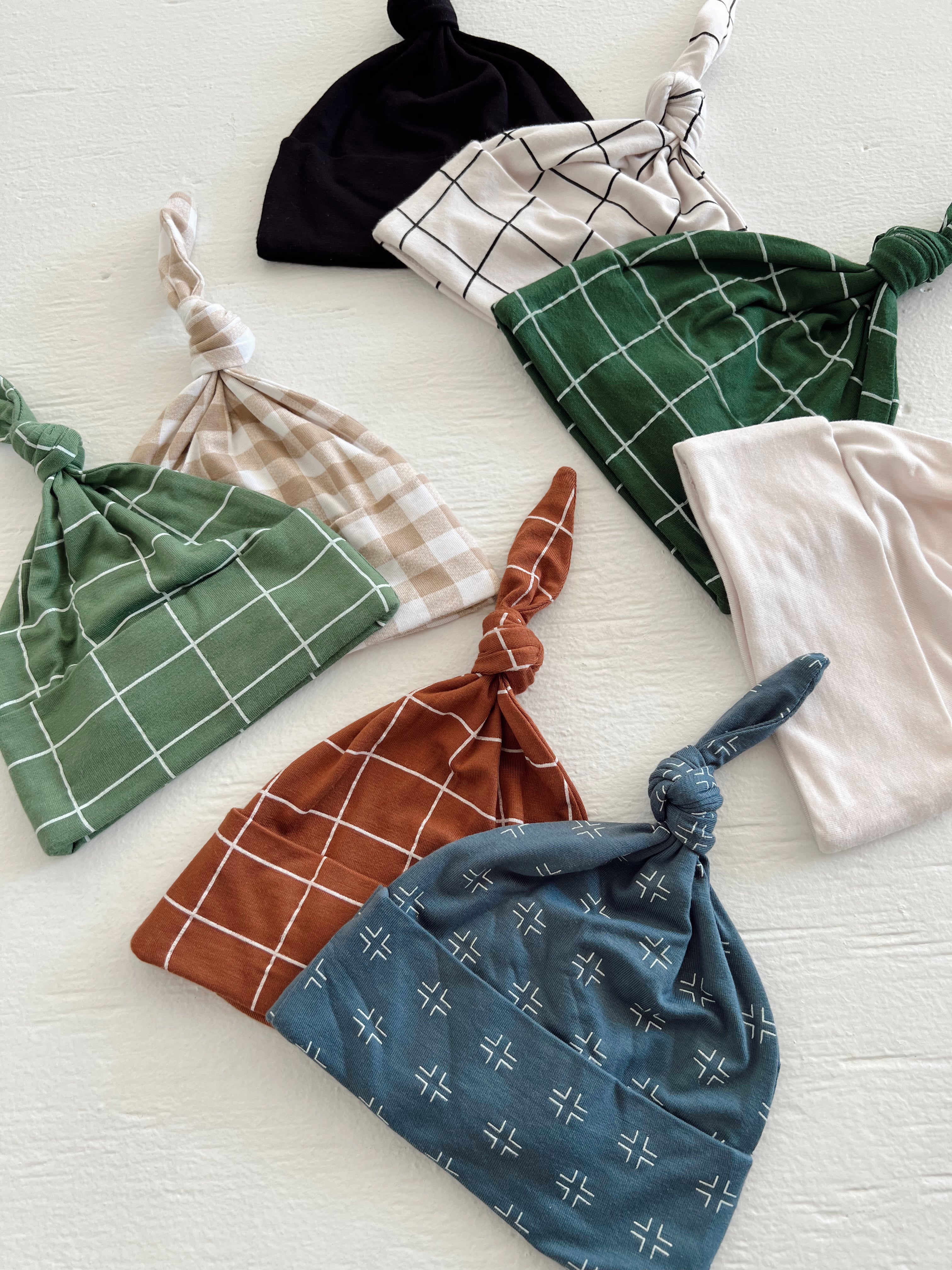 A collection of playful, patterned baby hats in various colors and designs, arranged on a light surface.