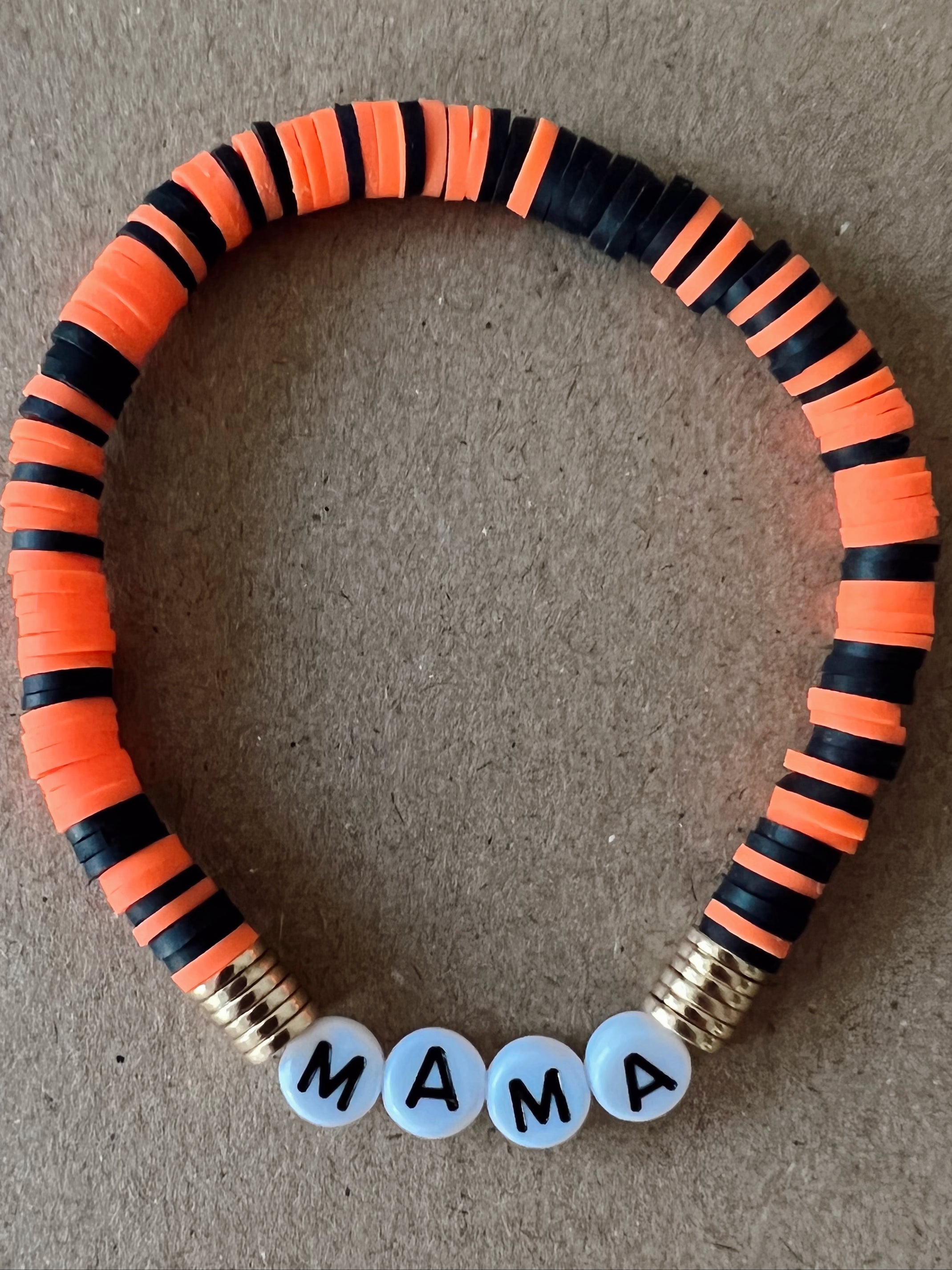 Colorful beaded bracelet with orange and black stripes, featuring the word "MAMA" in white beads.