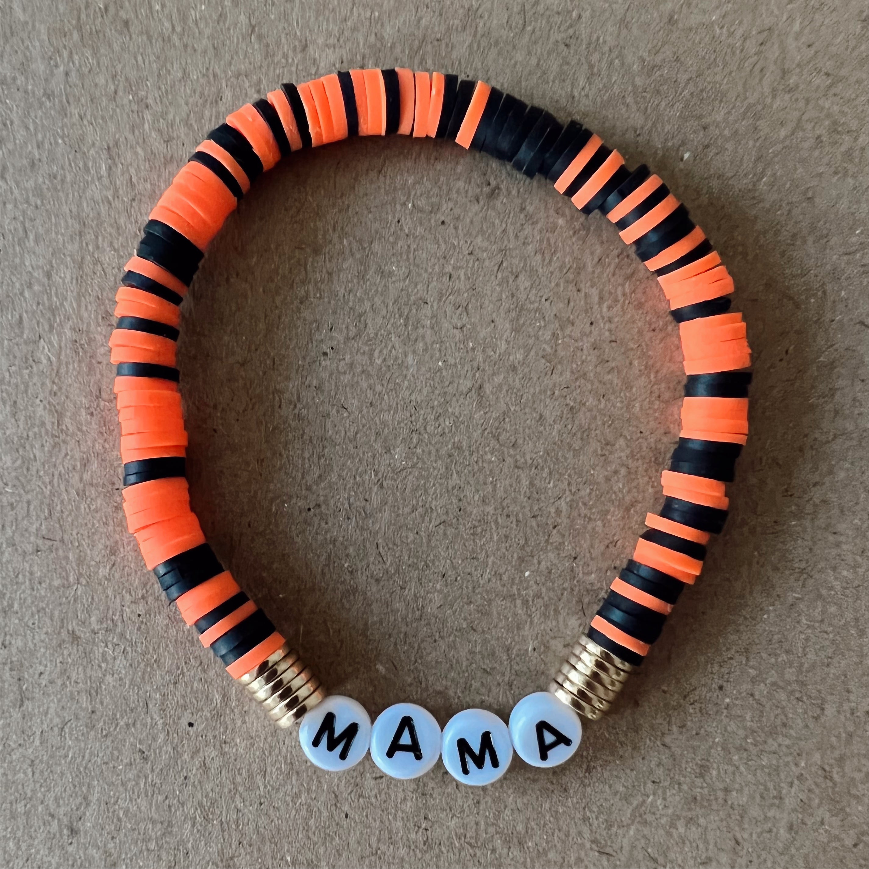 Colorful beaded bracelet with orange and black stripes, featuring the word "MAMA" in white beads.