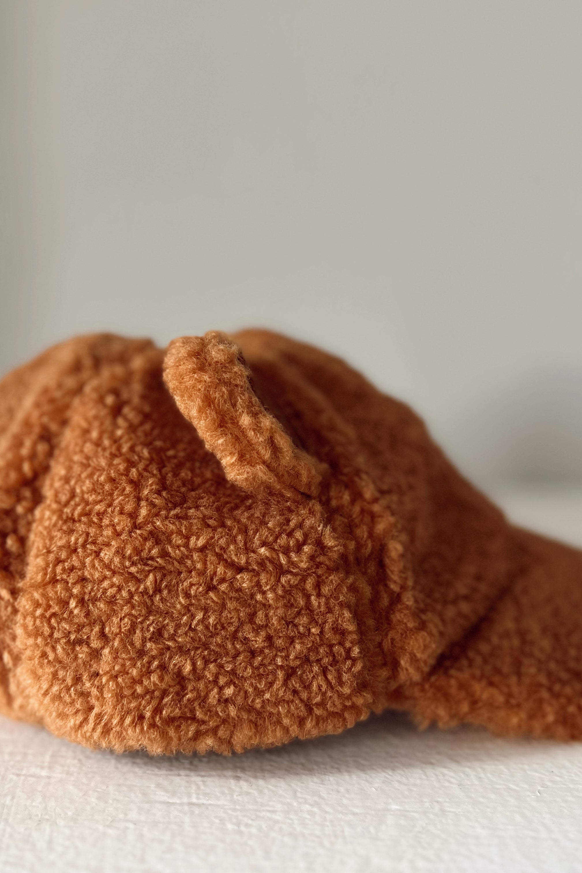 Soft, fluffy orange hat with a rounded top and curved brim, resting on a white surface.