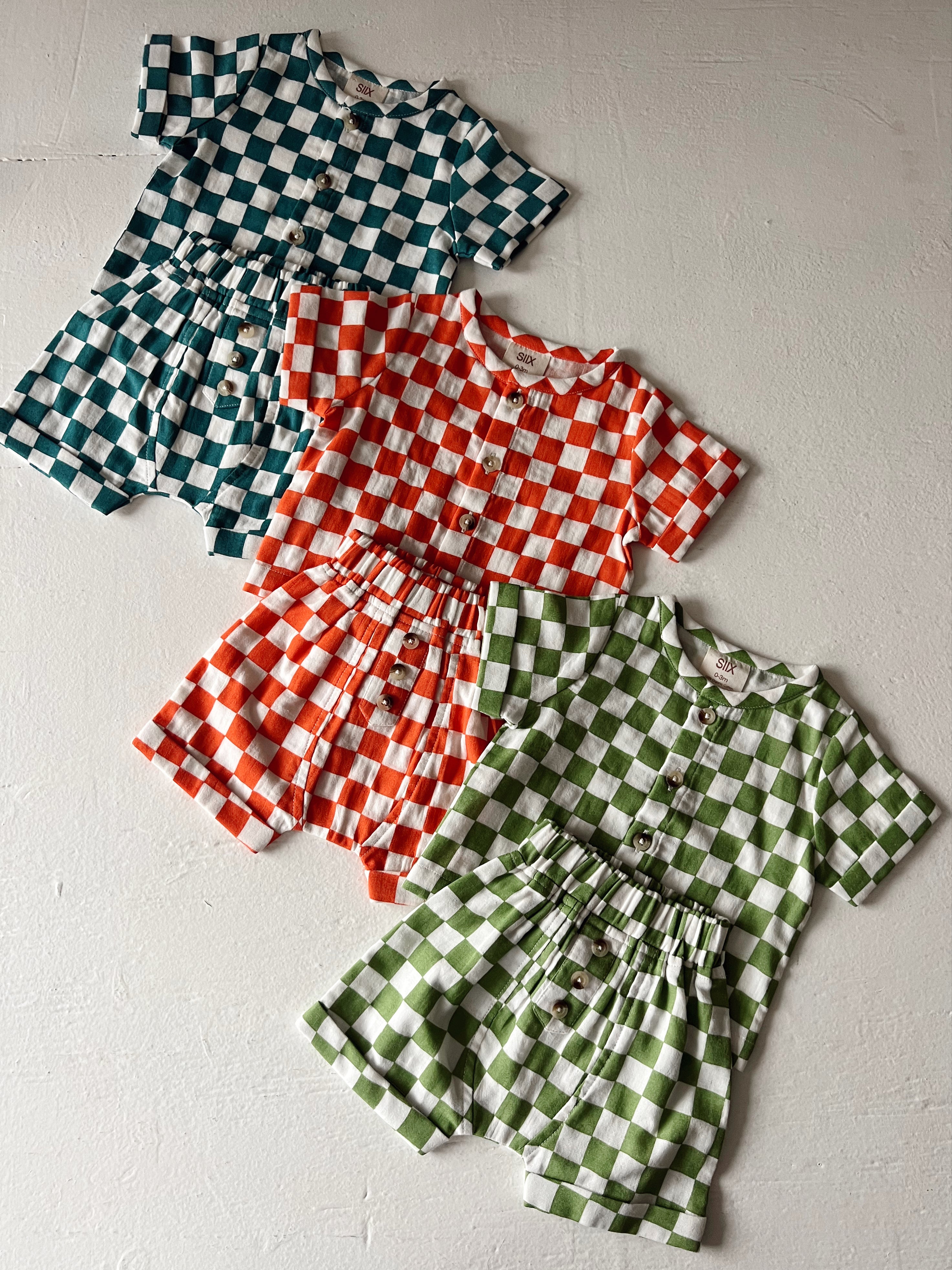 Colorful checkered outfits for children in green, orange, and teal displayed on a textured surface.