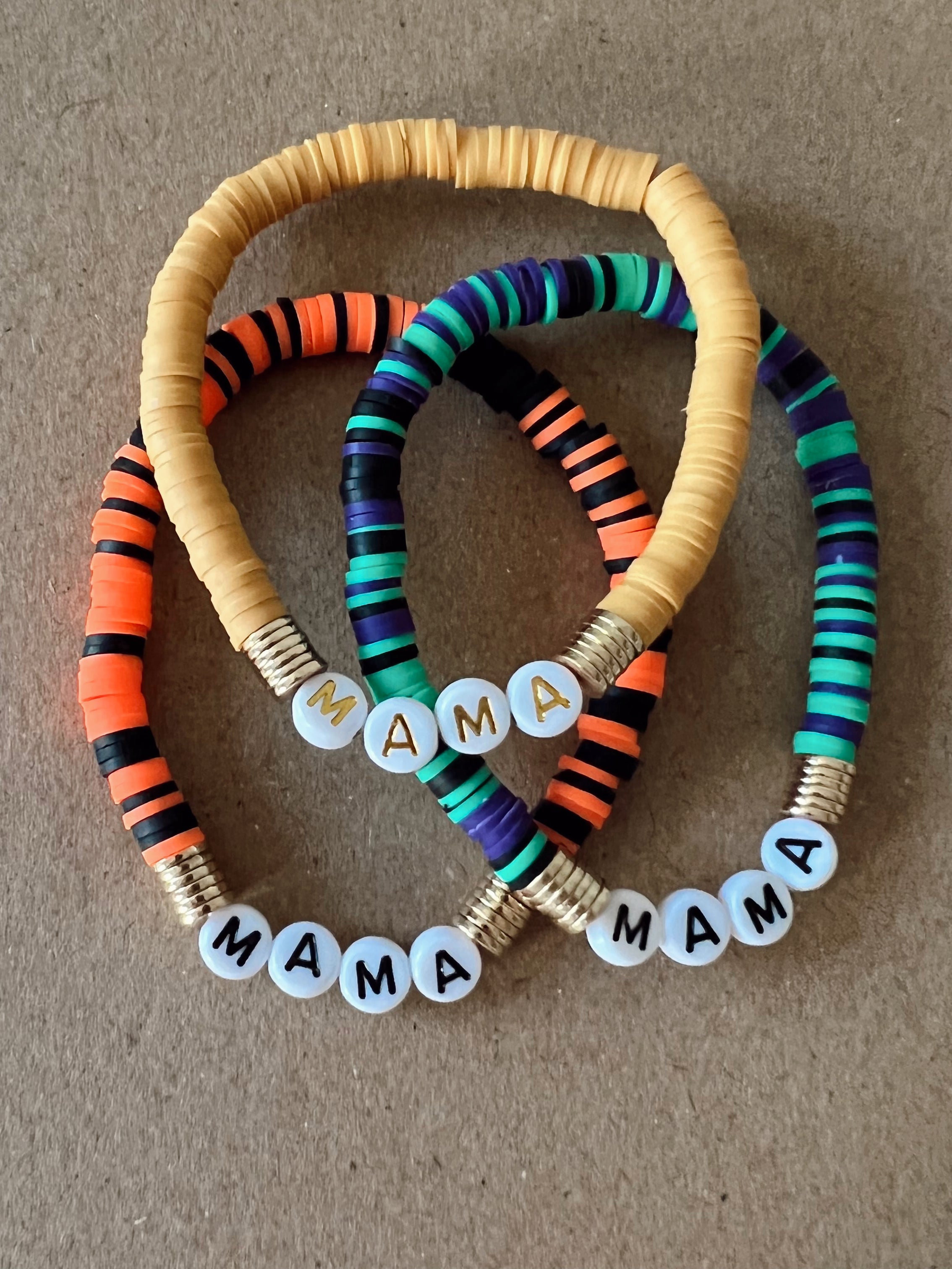 Colorful beaded bracelets with the word "MAMA" displayed on each, arranged on a brown background.