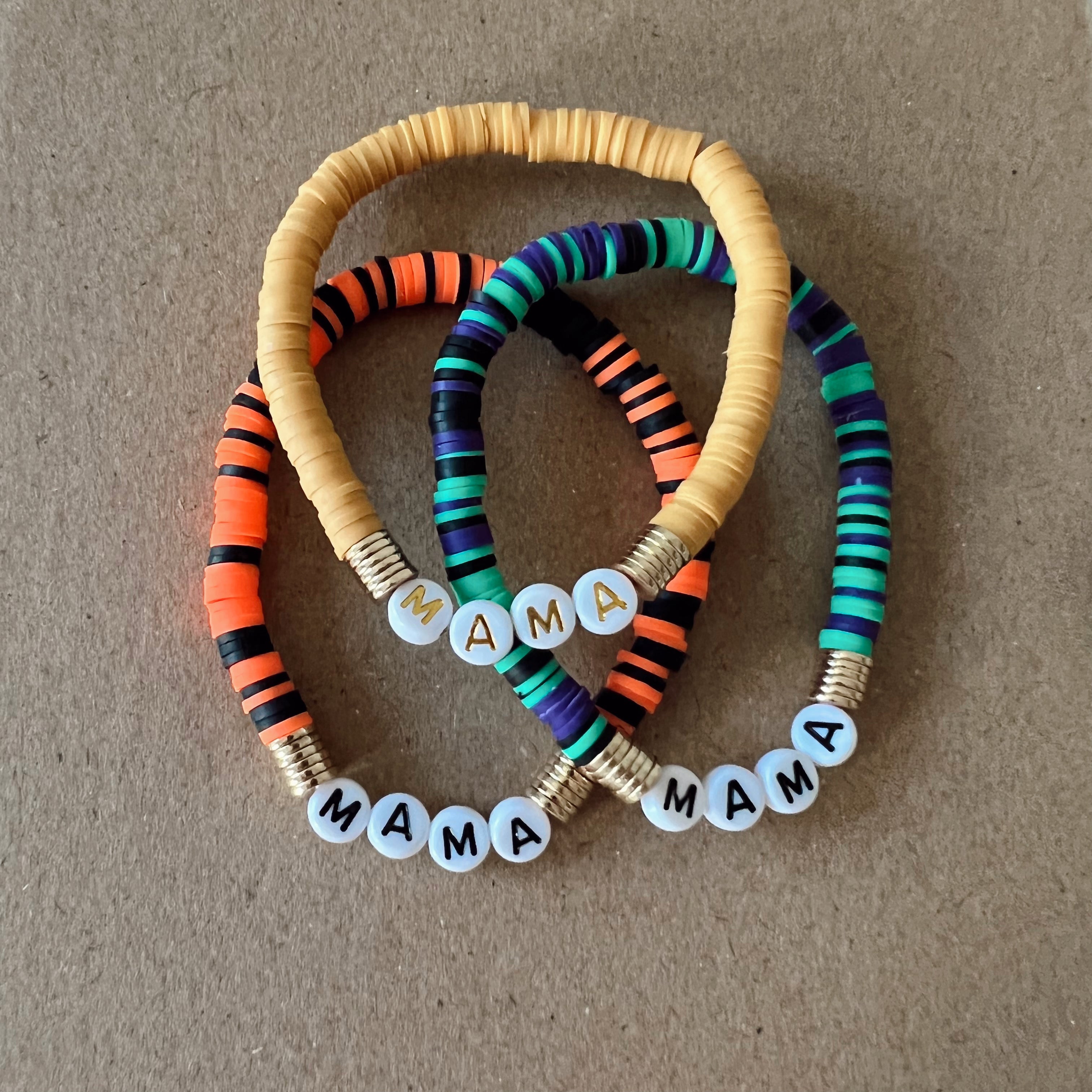 Colorful beaded bracelets with the word "MAMA" displayed on each, arranged on a brown background.