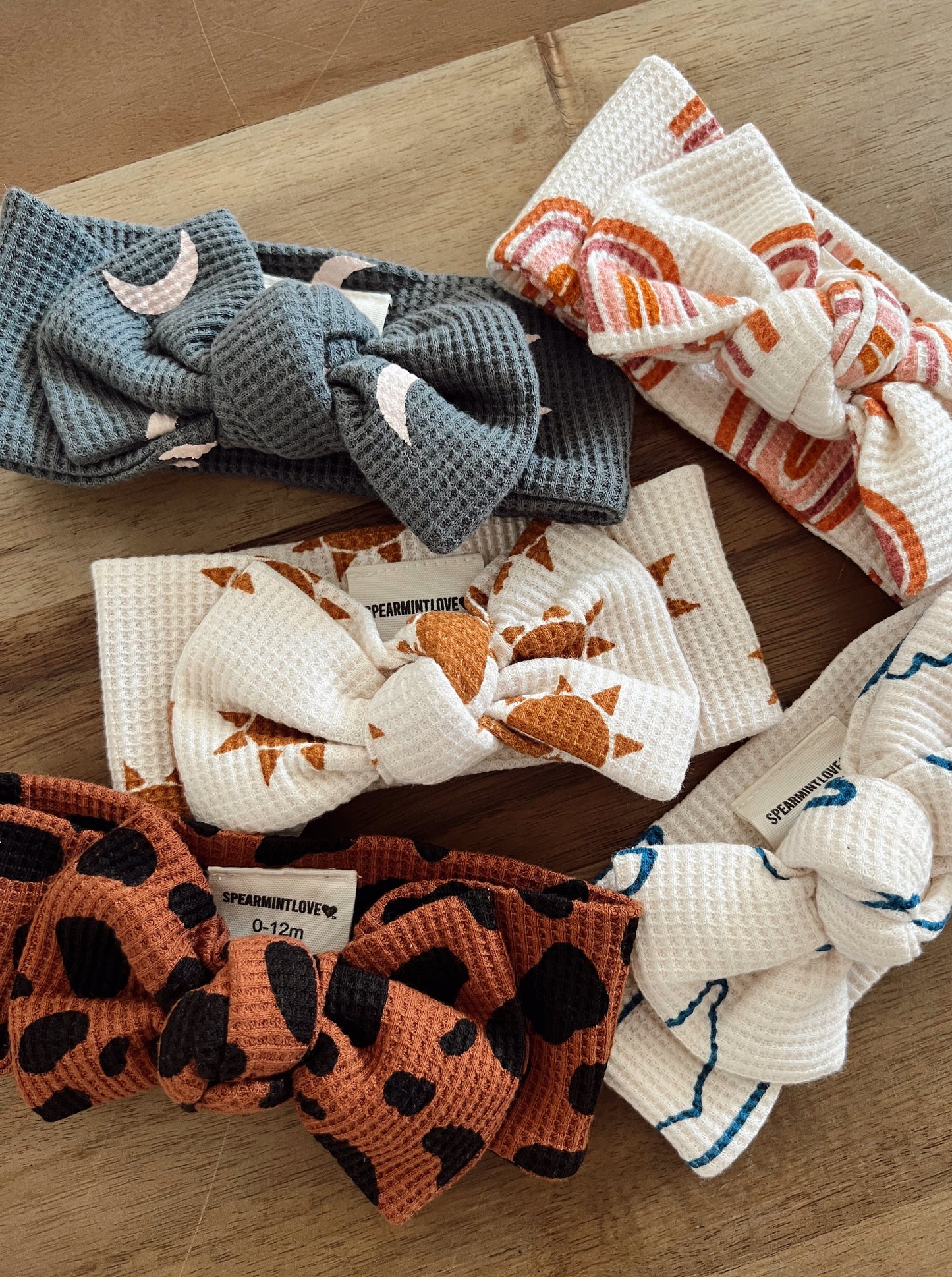 Five colorful baby headbands with various patterns on a wooden surface.