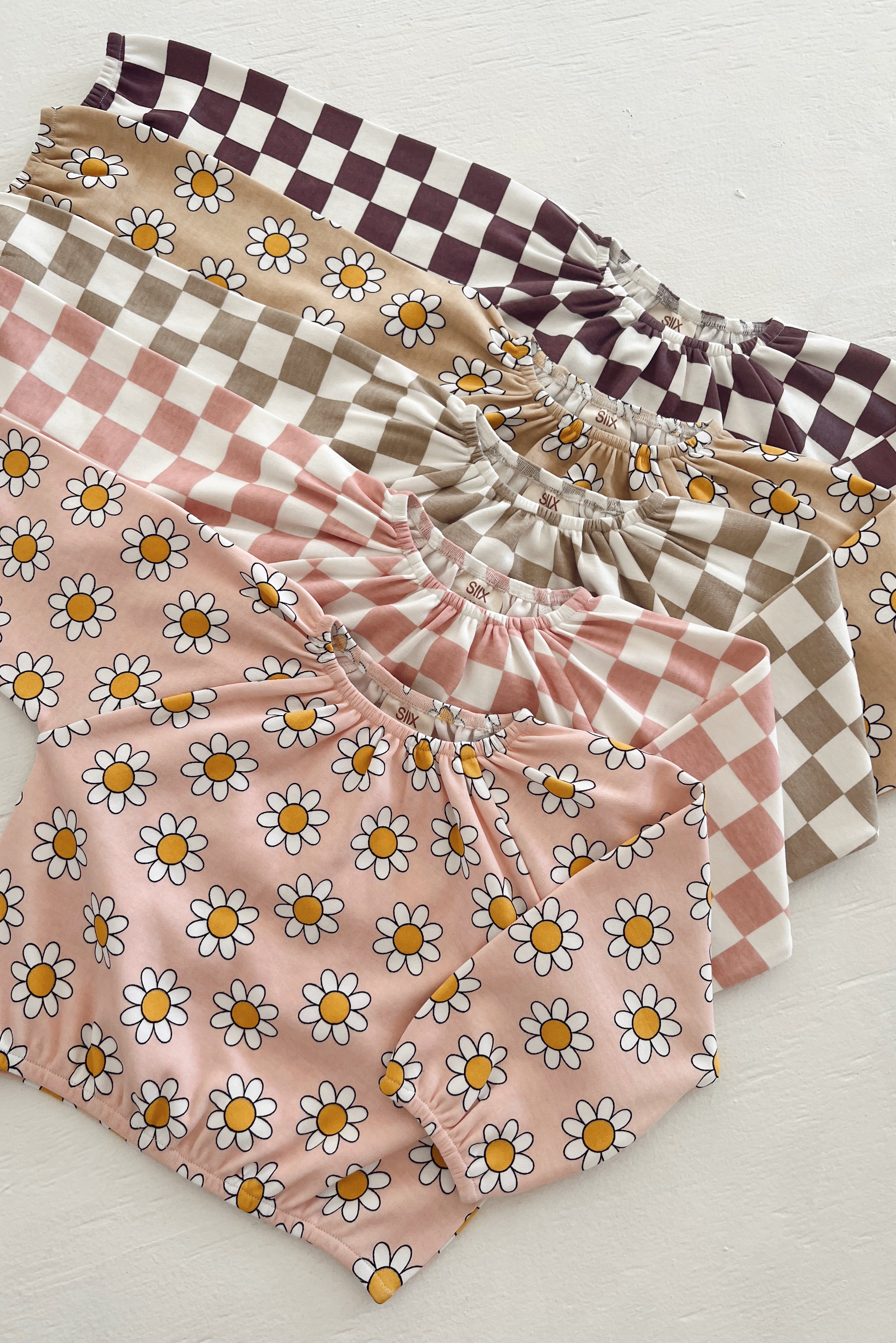 Five colorful blouses with floral and checked patterns laid on a white surface.