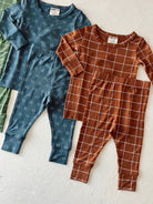 Colorful children's pajamas featuring blue patterned top and brown grid-patterned outfit, laid flat on a white surface.
