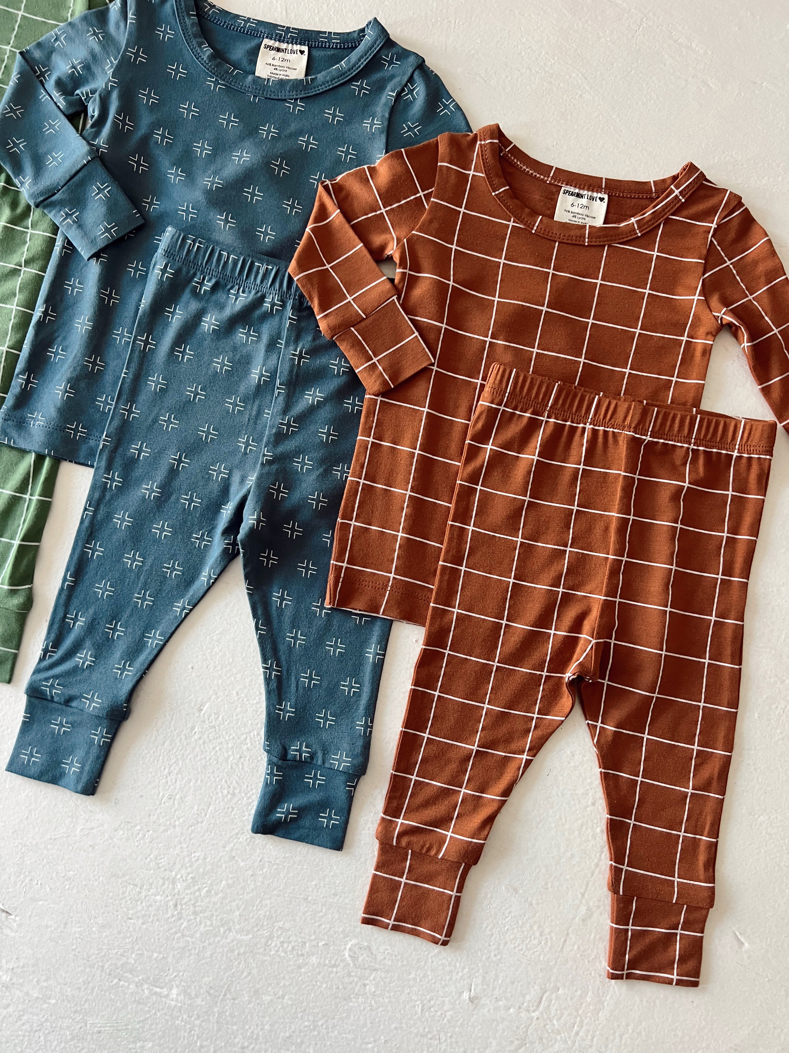 Colorful children's pajamas featuring blue patterned top and brown grid-patterned outfit, laid flat on a white surface.