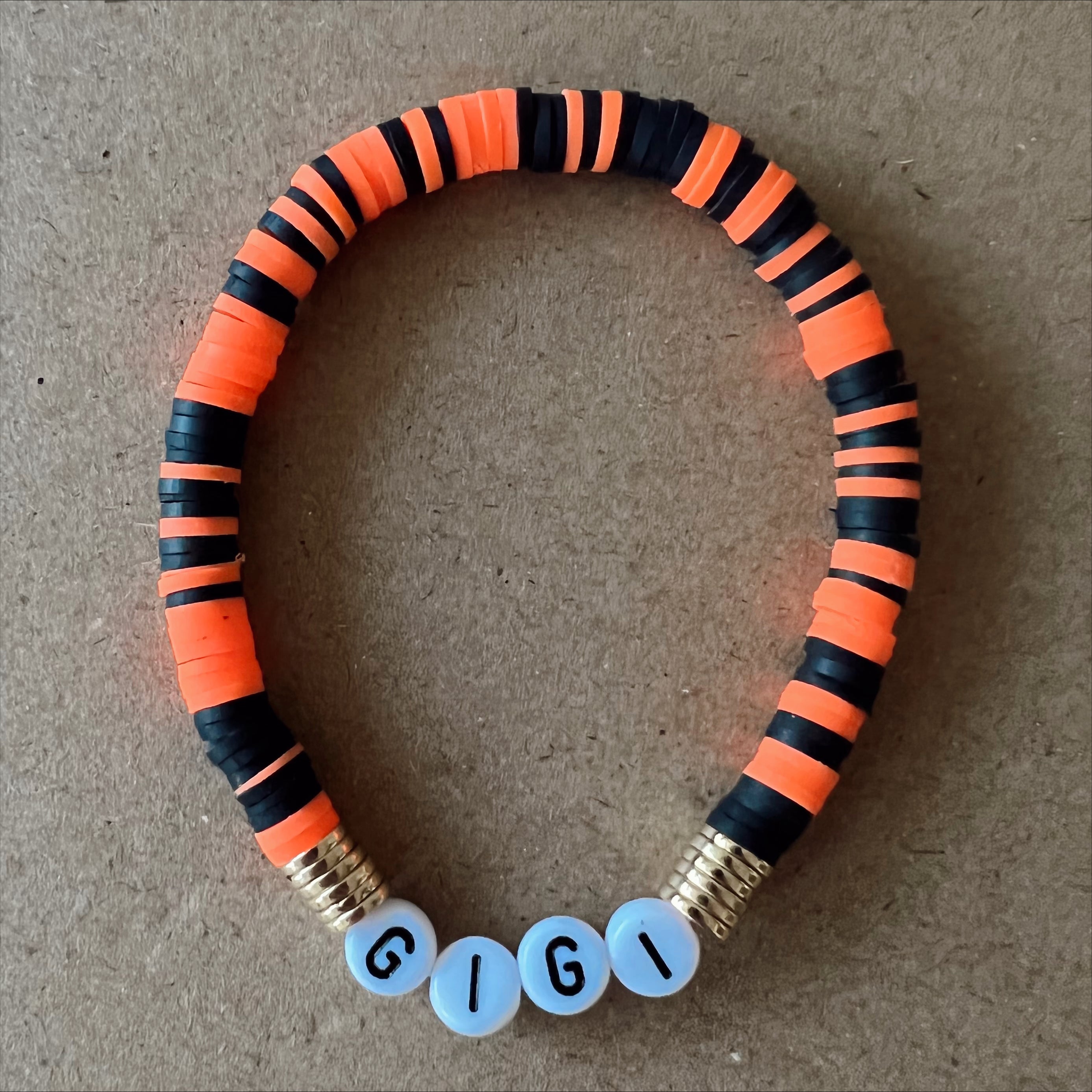 Colorful beaded bracelet with orange and black stripes, featuring the name "GIGI" in white letters.