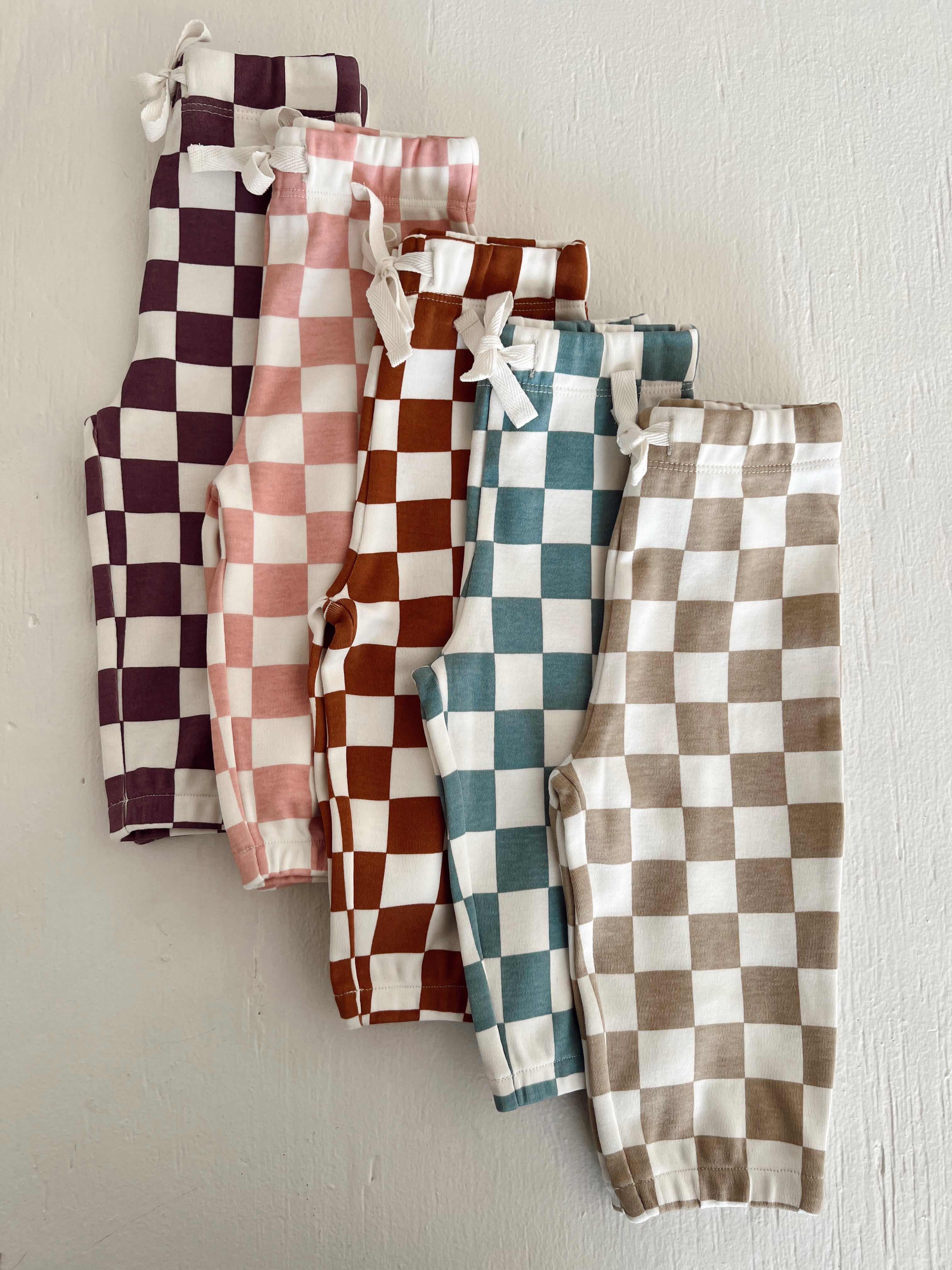 Colorful checkered pants in purple, pink, brown, teal, and beige arranged in a row on a light background.