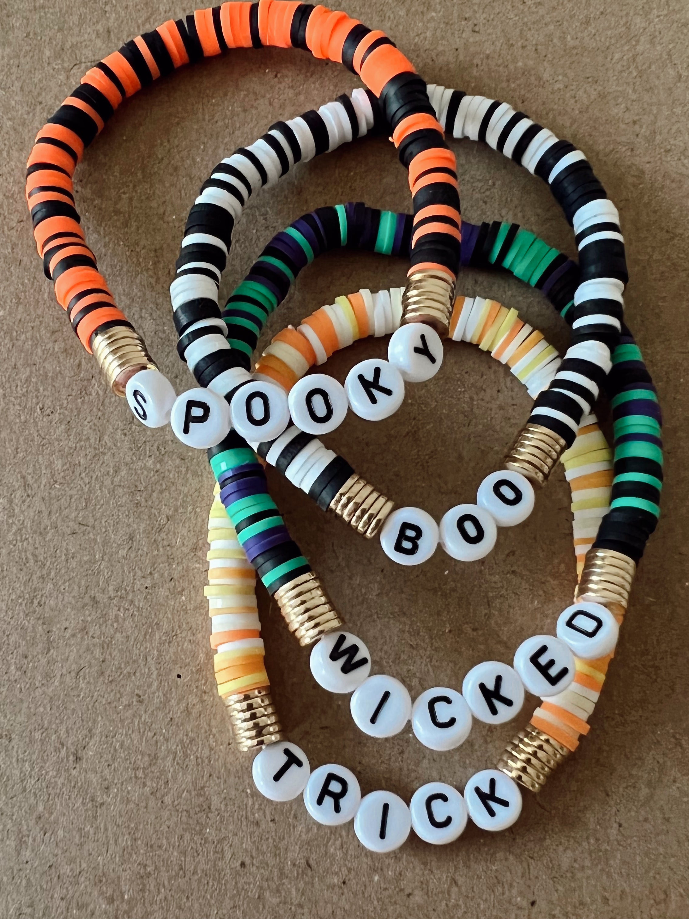 Colorful Halloween-themed bracelets with the words "Spooky," "Boo," "Wicked," and "Trick" on white beads.