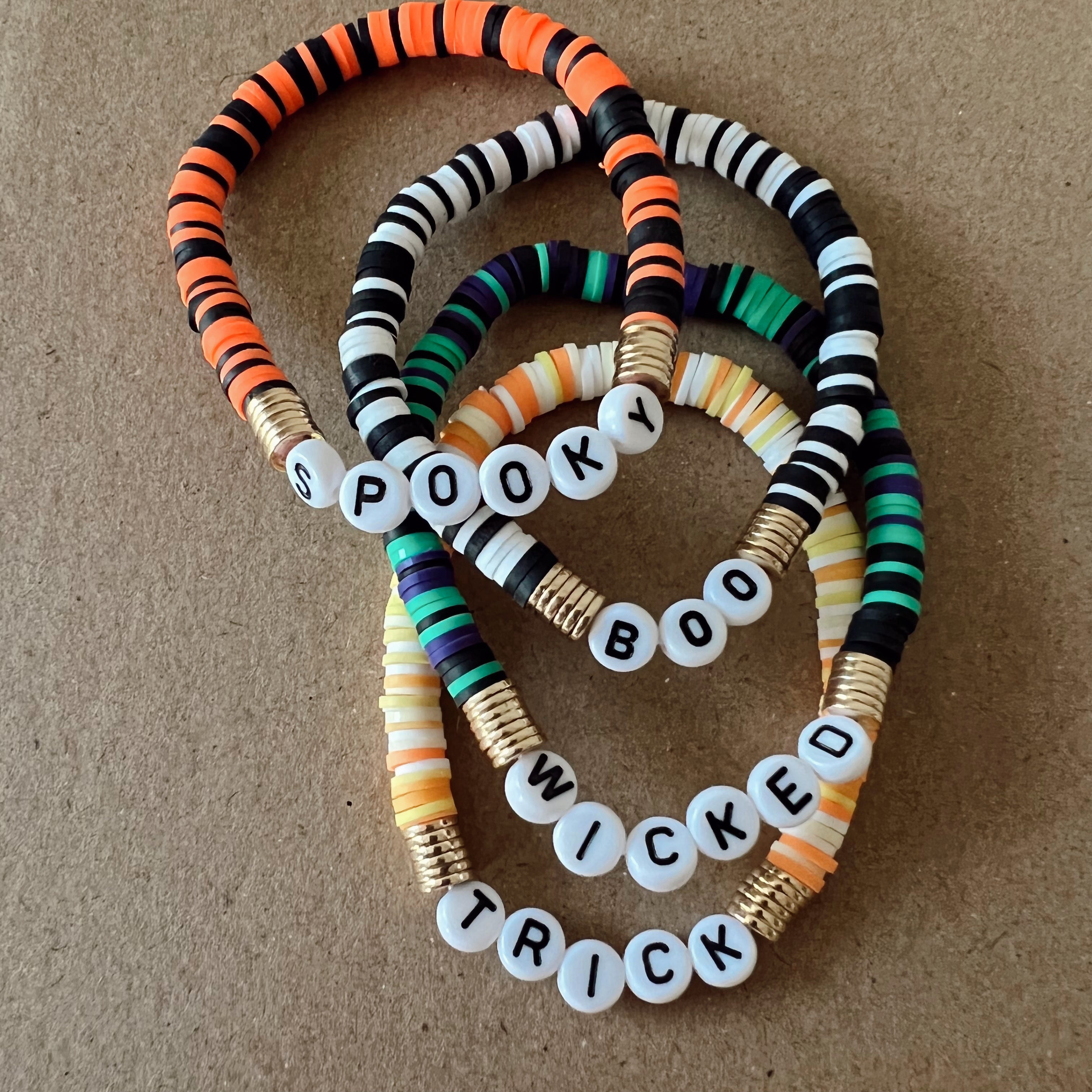 Colorful Halloween-themed bracelets with the words "Spooky," "Boo," "Wicked," and "Trick" on white beads.