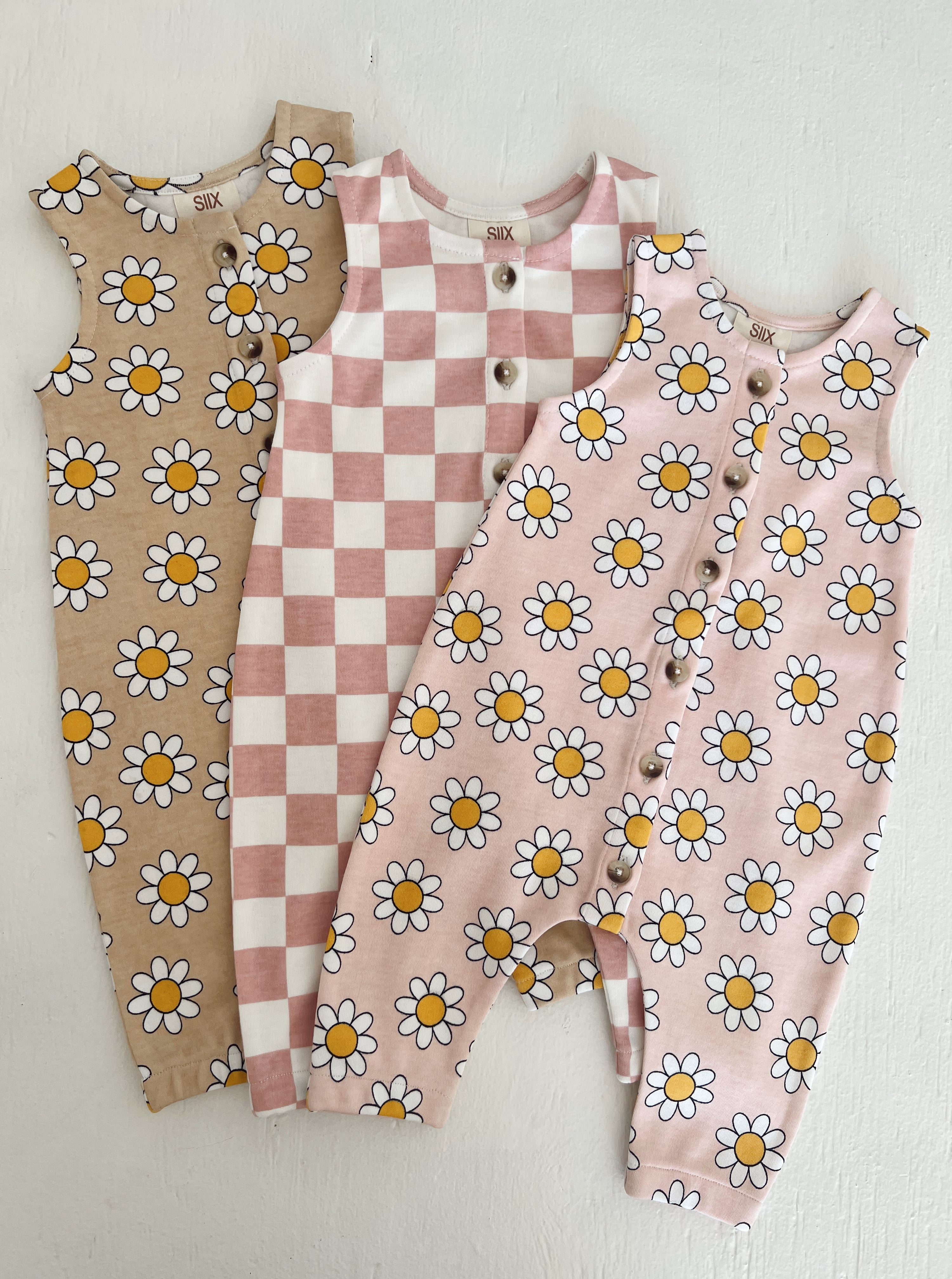 Three toddler rompers featuring floral and checkered patterns in neutral and pastel colors.